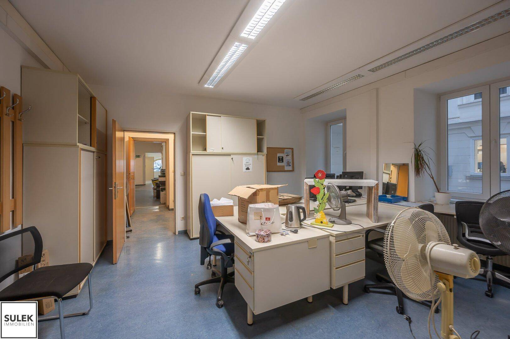 Weitläufiges Büro mit mehreren Schreibtischen, Büromöbeln und Fenstern, die den Raum erhellen.