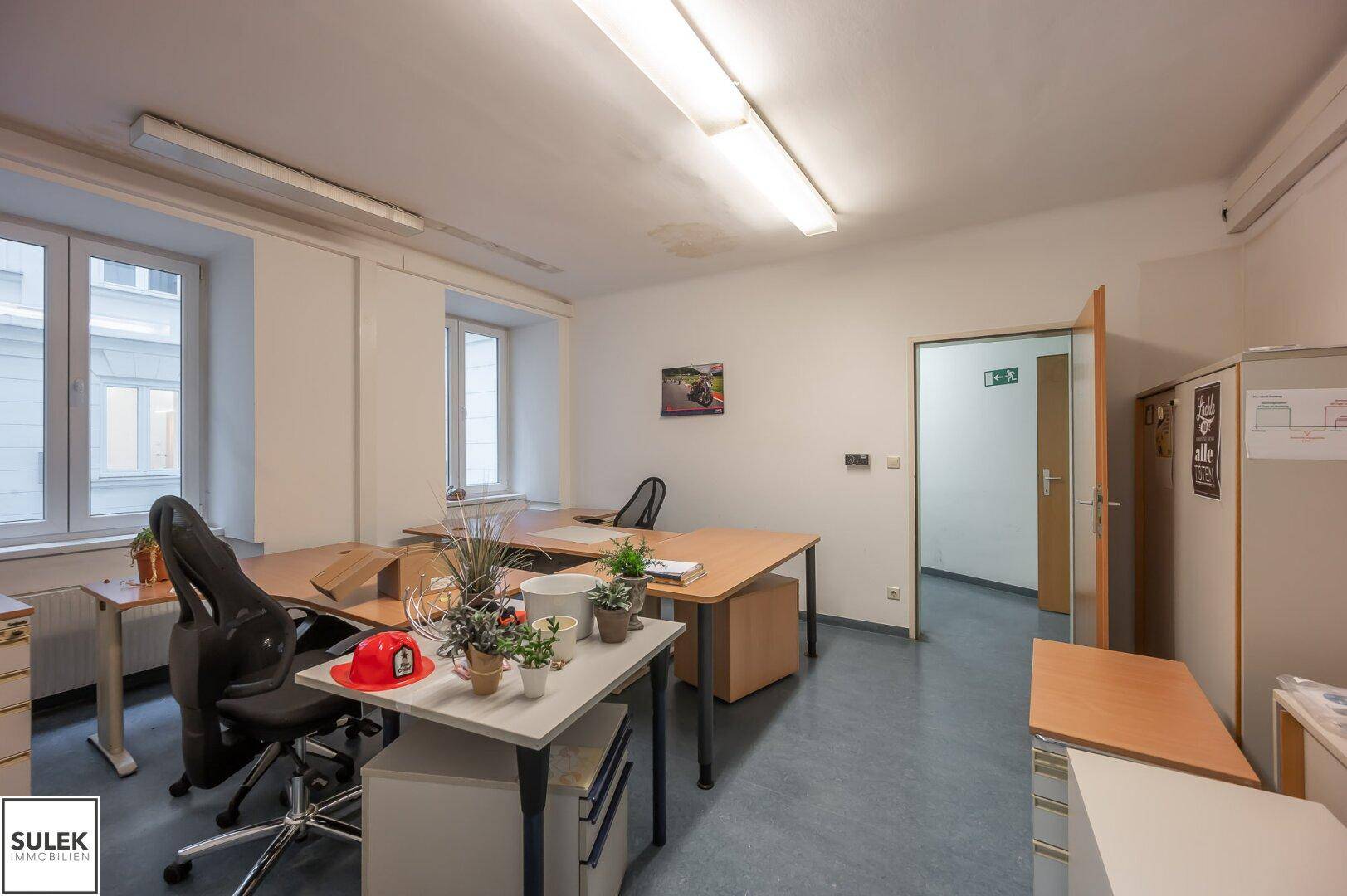 Helles Büro mit mehreren Arbeitsplätzen, Bürostühlen und Fenstern, die Tageslicht hereinlassen.