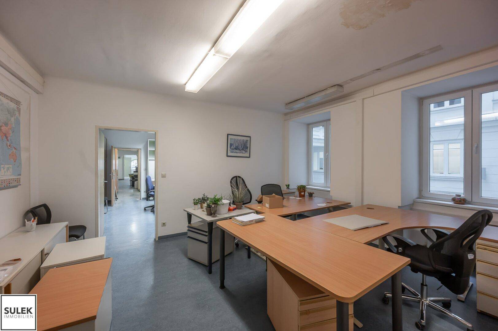 Geräumiges Büro mit mehreren Arbeitsplätzen, Aktenschränken und großen Fenstern für viel Tageslicht.