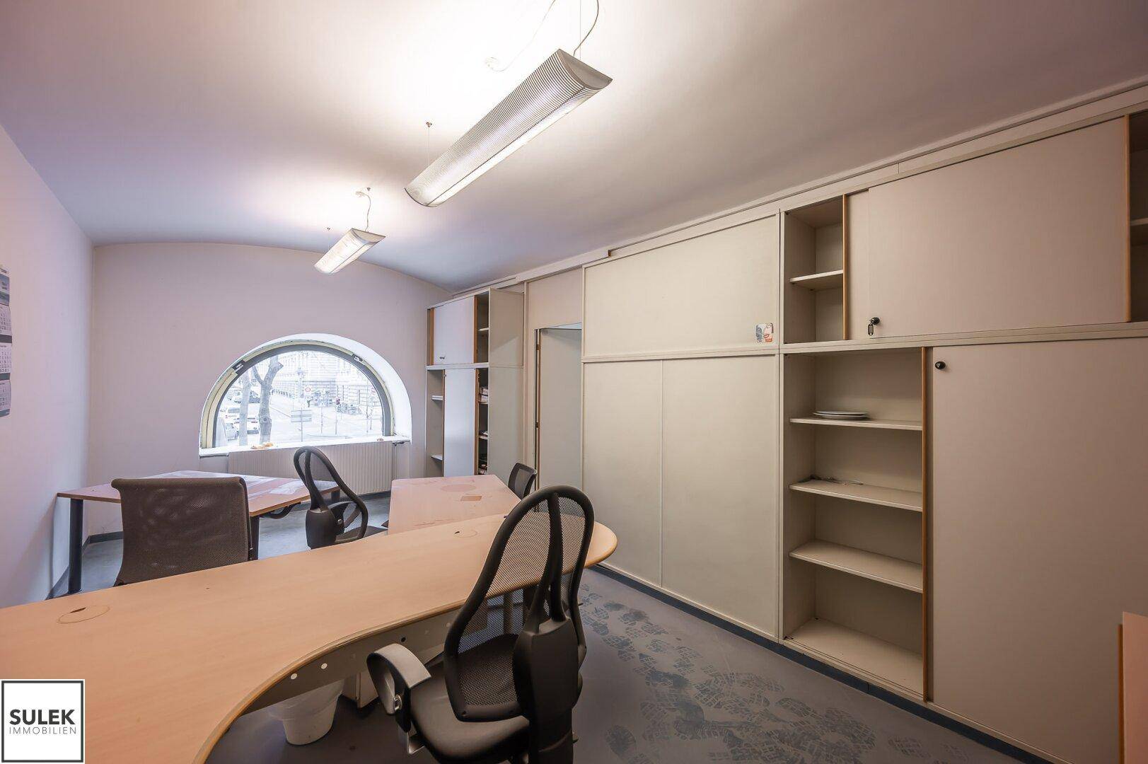 Geräumiges Büro mit gewölbten Fenstern, Einbauschränken und mehreren Arbeitsplätzen.