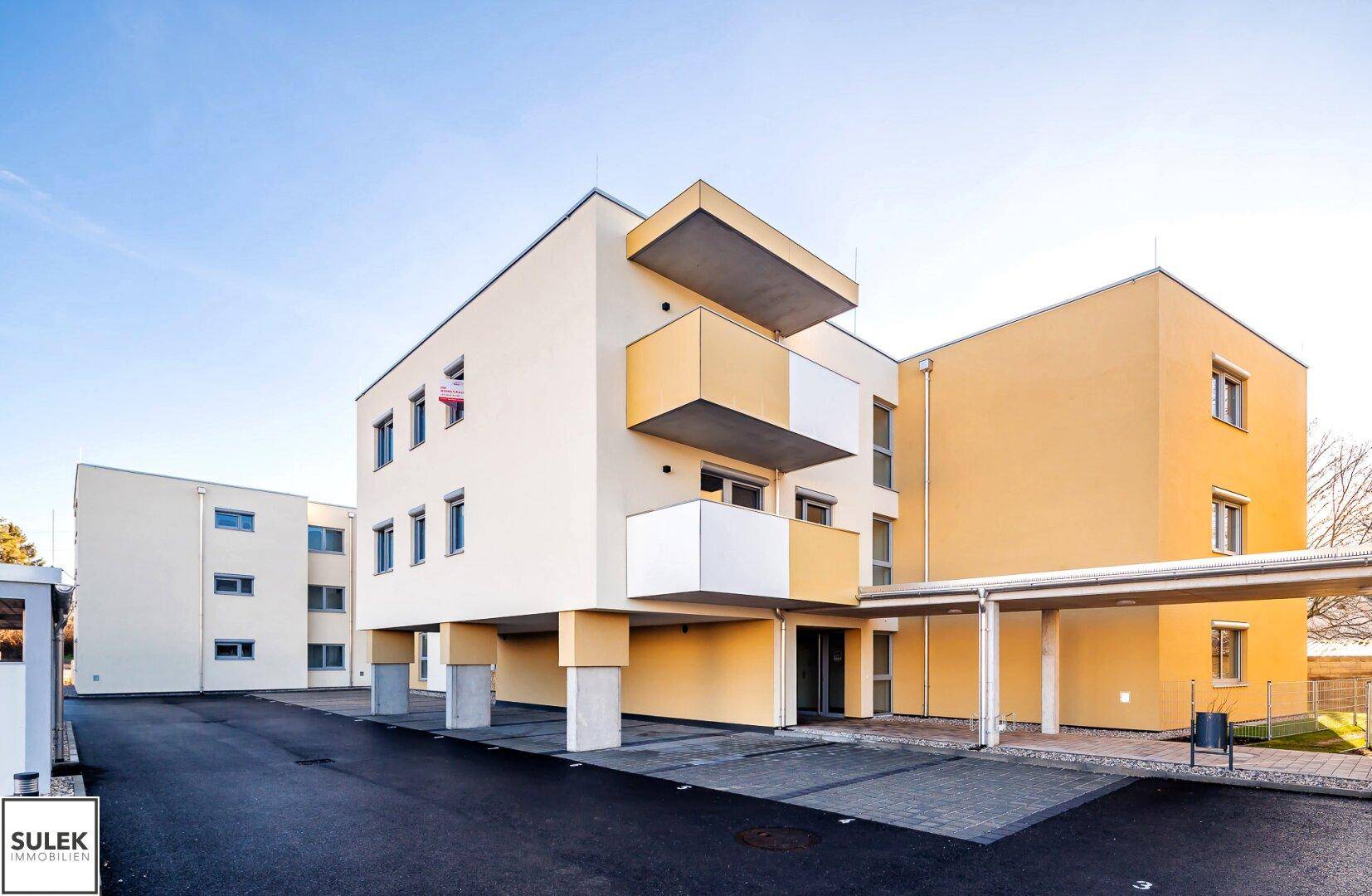 Modernes Wohngebäude mit heller Fassade, Balkonen und einem überdachten Carport-Bereich.