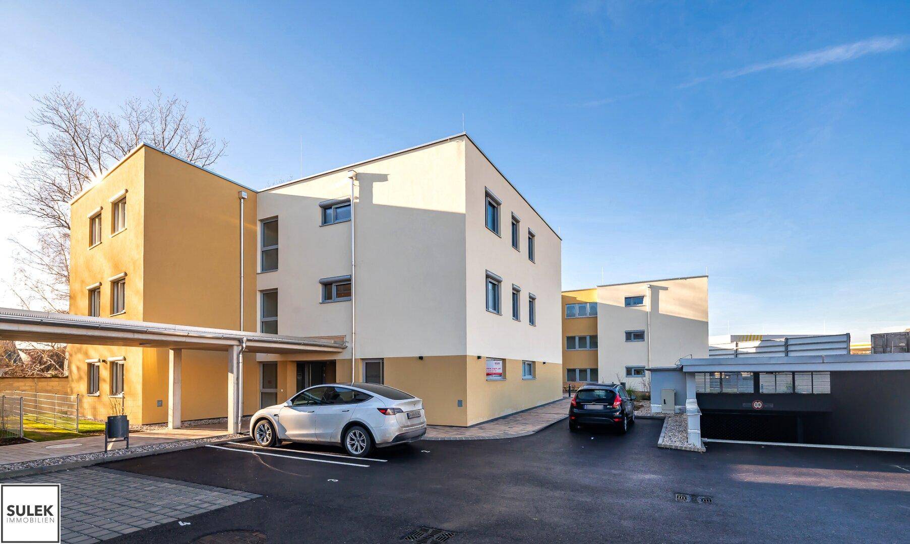 Moderne Wohngebäude mit heller Fassade, Carport und Parkplätzen.