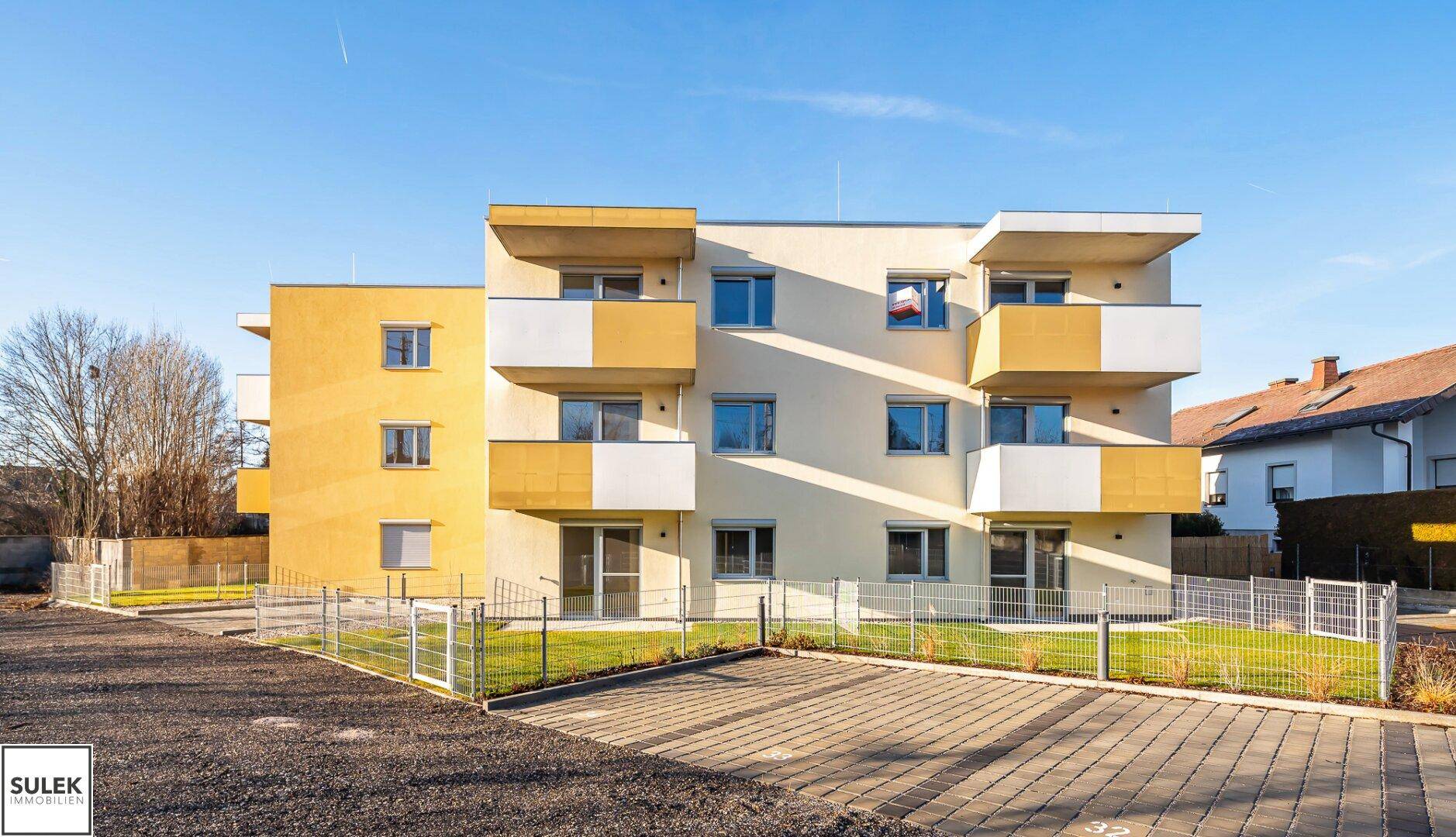 Frontansicht eines modernen Wohngebäudes mit Balkonen und einem Parkplatz im Vordergrund.