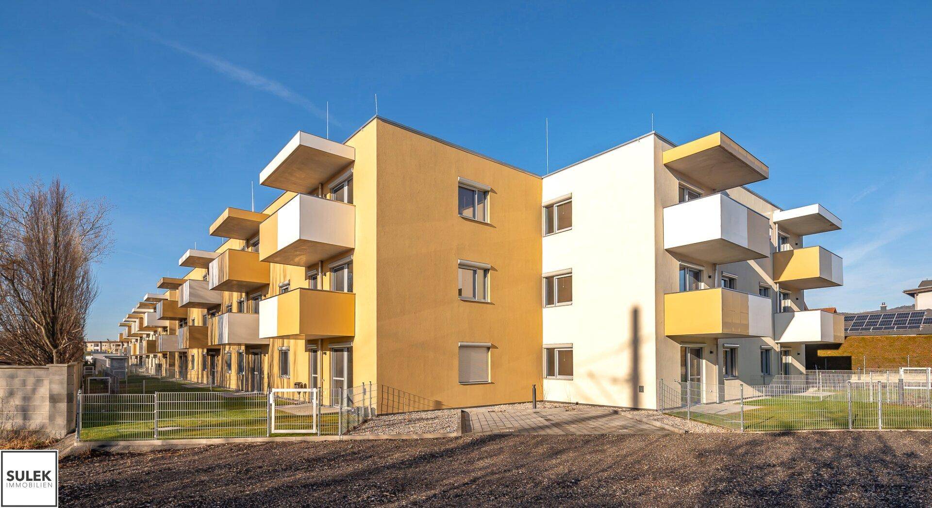 Reihe moderner Wohngebäude mit gelben und weißen Fassaden sowie Balkonen unter blauem Himmel.
