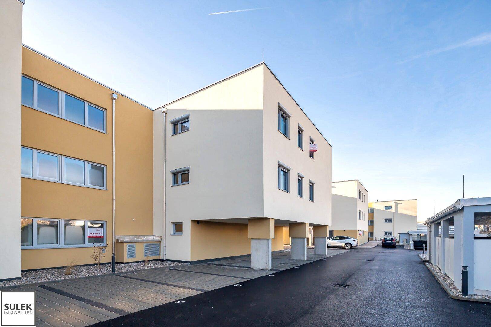 Moderne Wohngebäude mit heller Fassade und einem überdachten Parkplatzbereich.