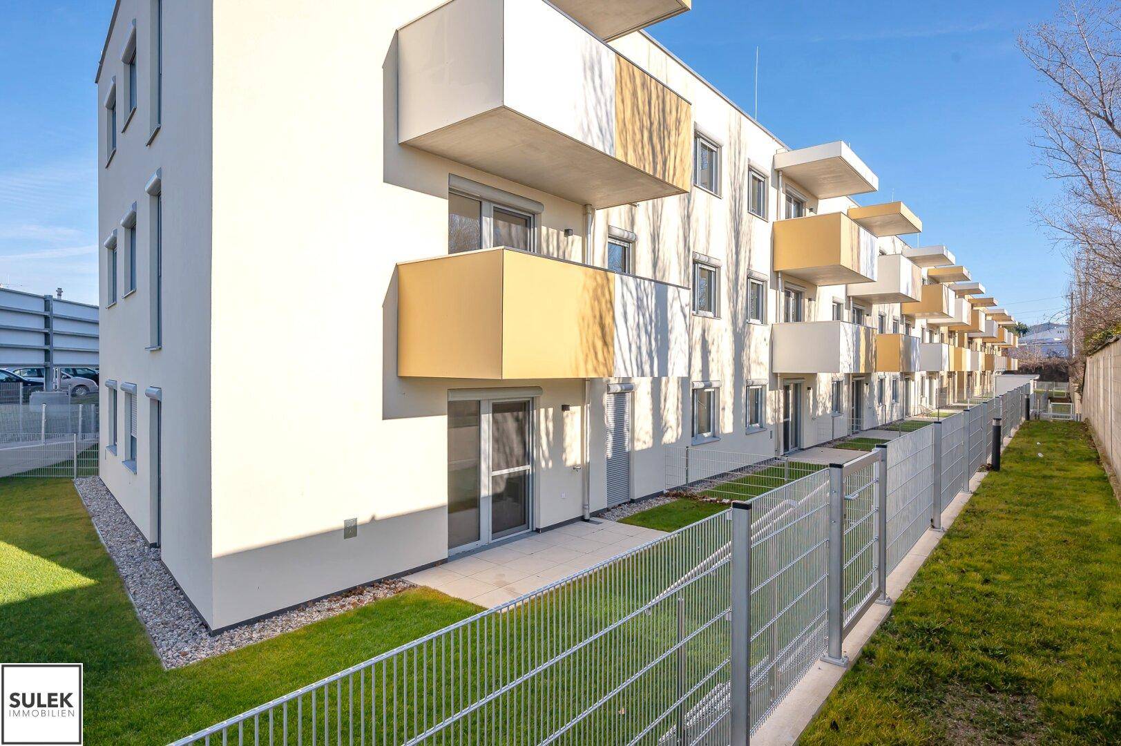 Reihe moderner Wohngebäude mit Terrassen im Erdgeschoss und umzäunten Grünflächen.