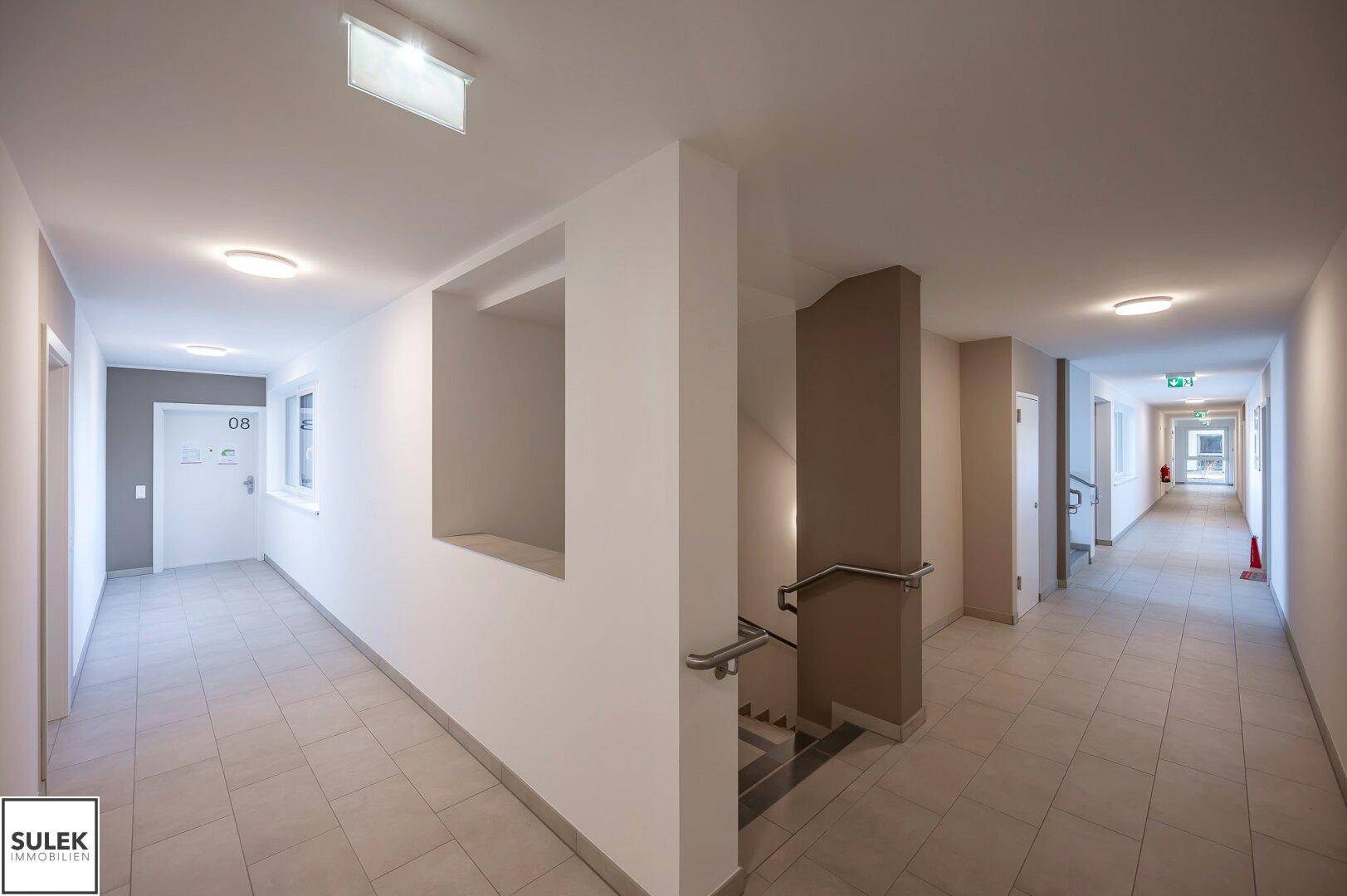 Heller Flur im Mehrfamilienhaus mit Fliesenboden und Treppenaufgang.