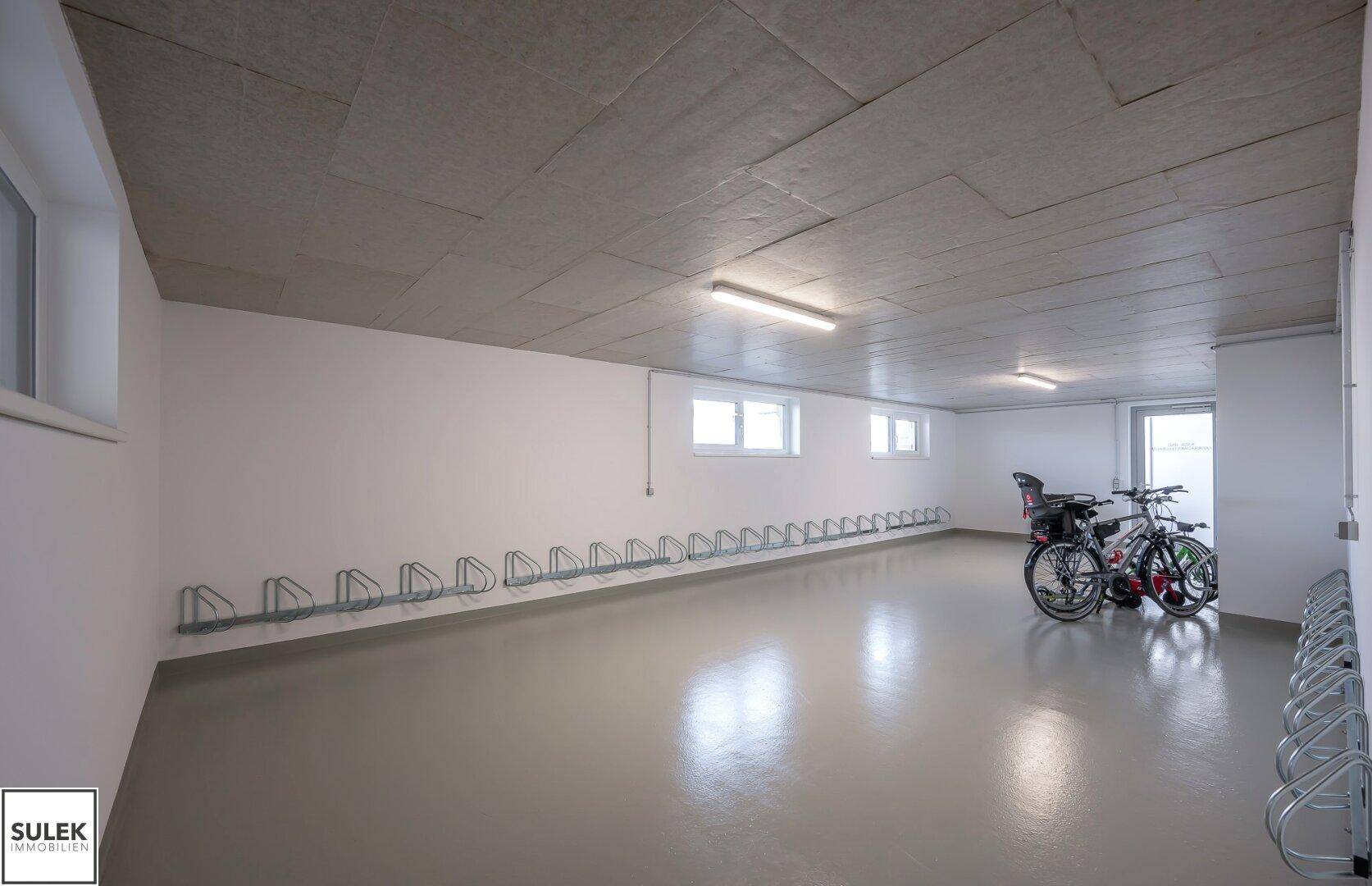 Geräumiger Fahrradraum im Untergeschoss mit zahlreichen Fahrradständern und Fenstern.