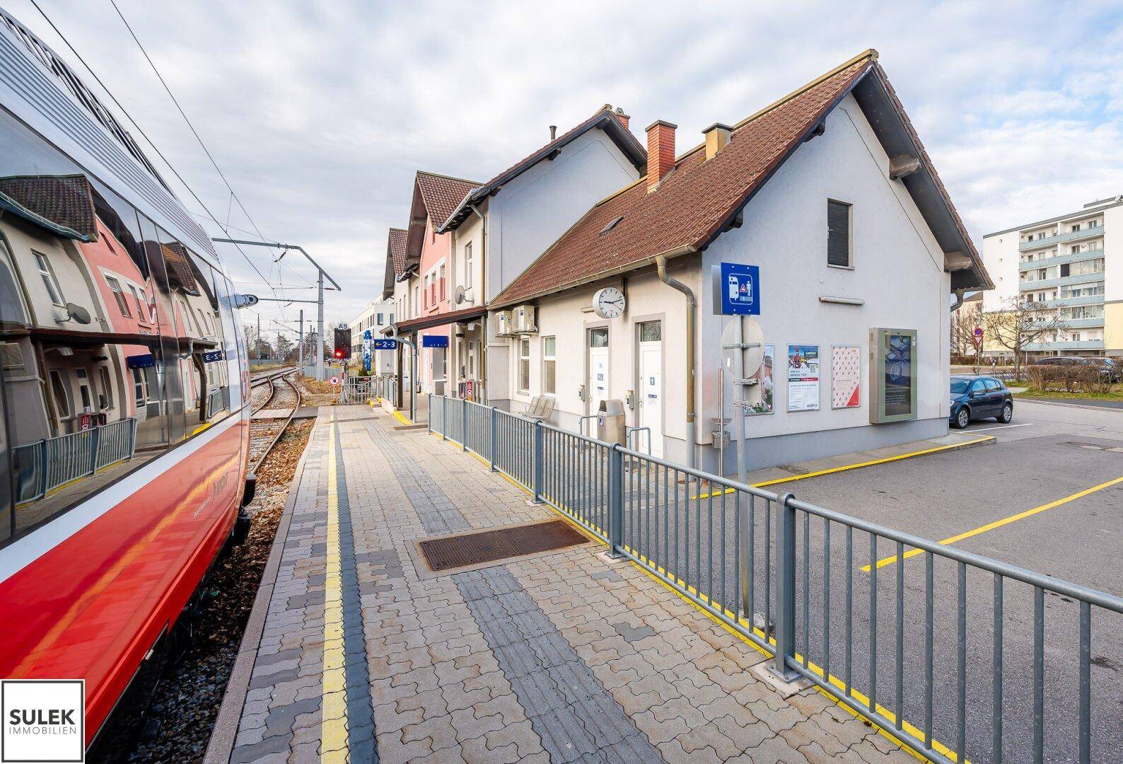 Ansicht des Bahnhofsgebäudes in Eisenstadt mit einem haltenden Zug am Bahnsteig.