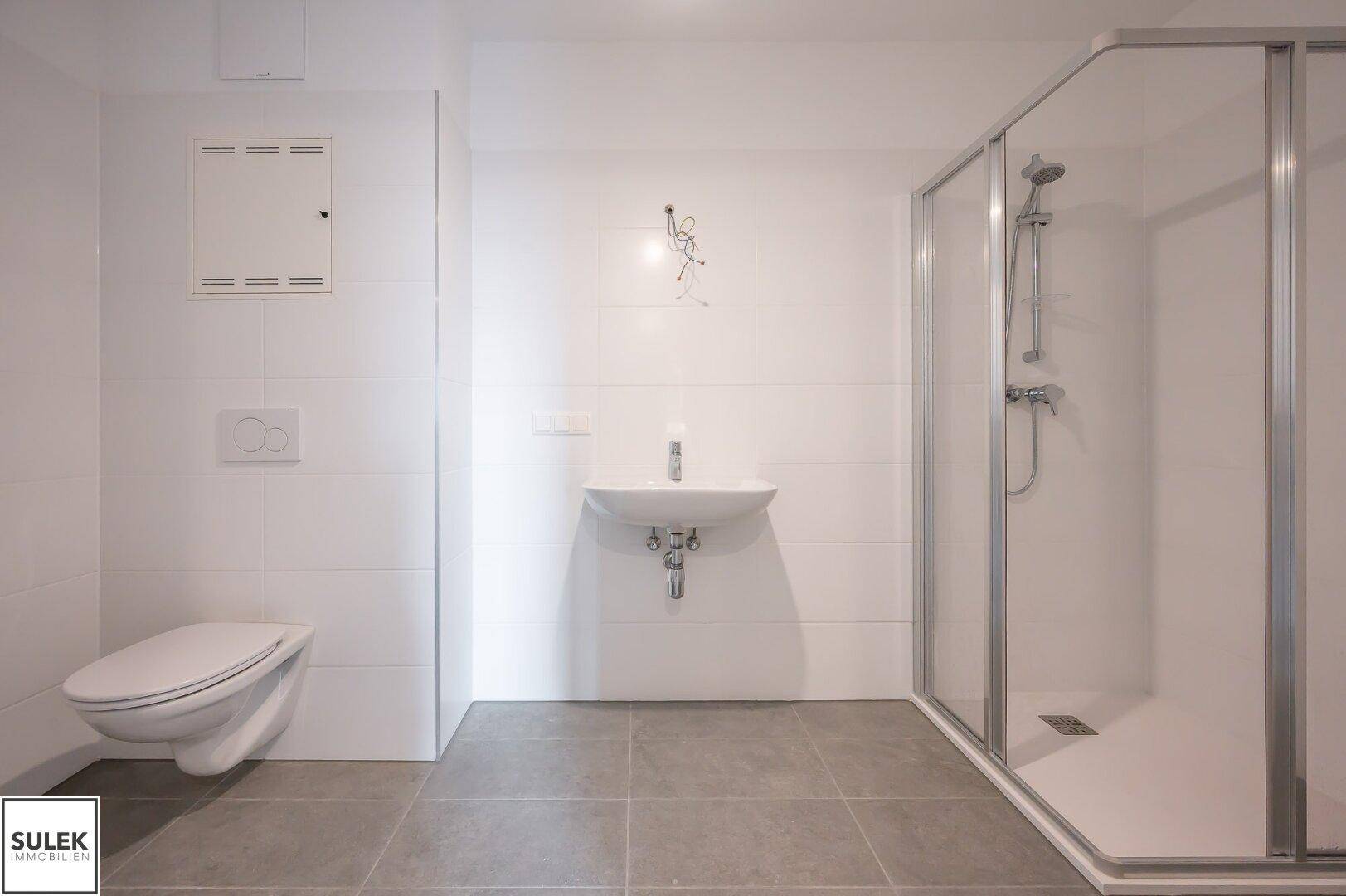 Helles Badezimmer mit Duschkabine, wandhängendem WC und modernem Waschbecken.