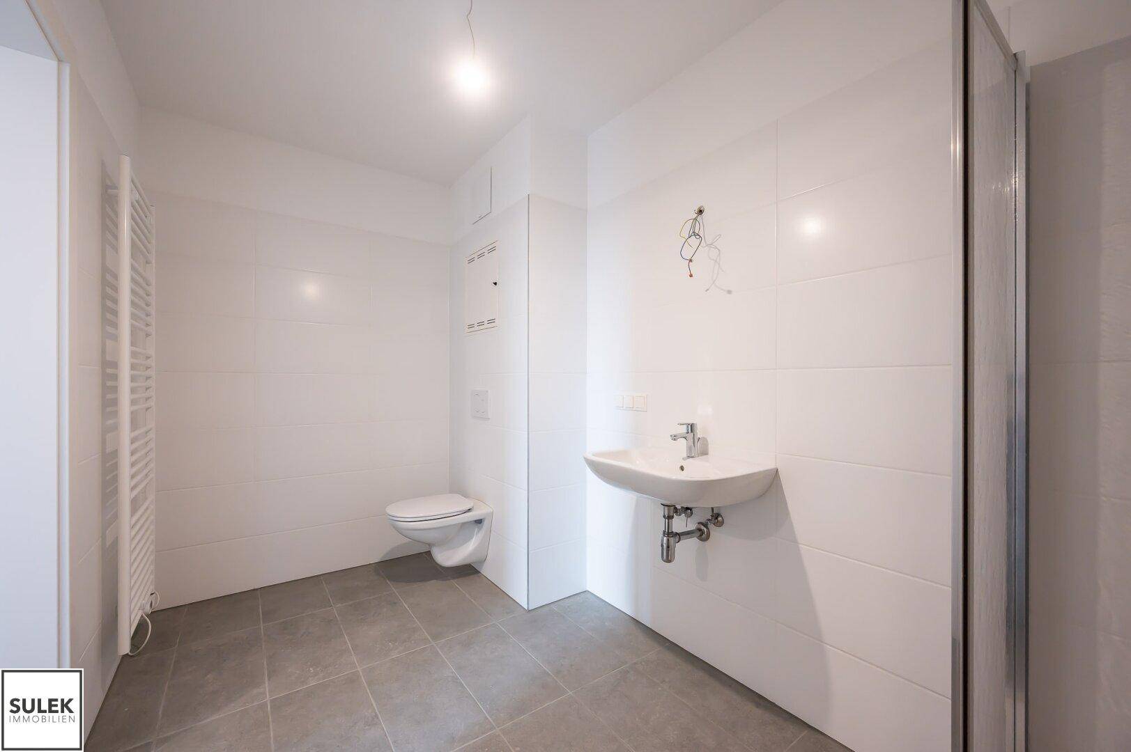 Modernes Badezimmer mit weißen Fliesen, Dusche, WC und Handtuchheizkörper.