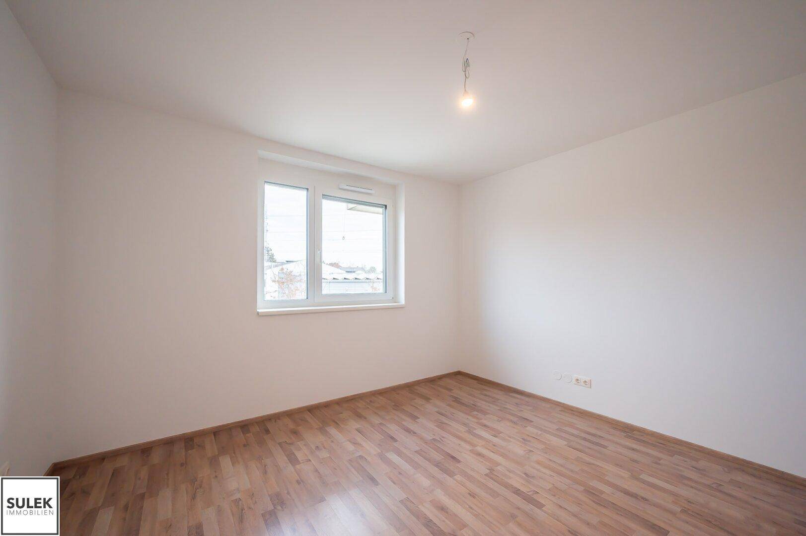 Leeres Schlafzimmer mit Laminatboden und einem Fenster, bereit zur individuellen Gestaltung.
