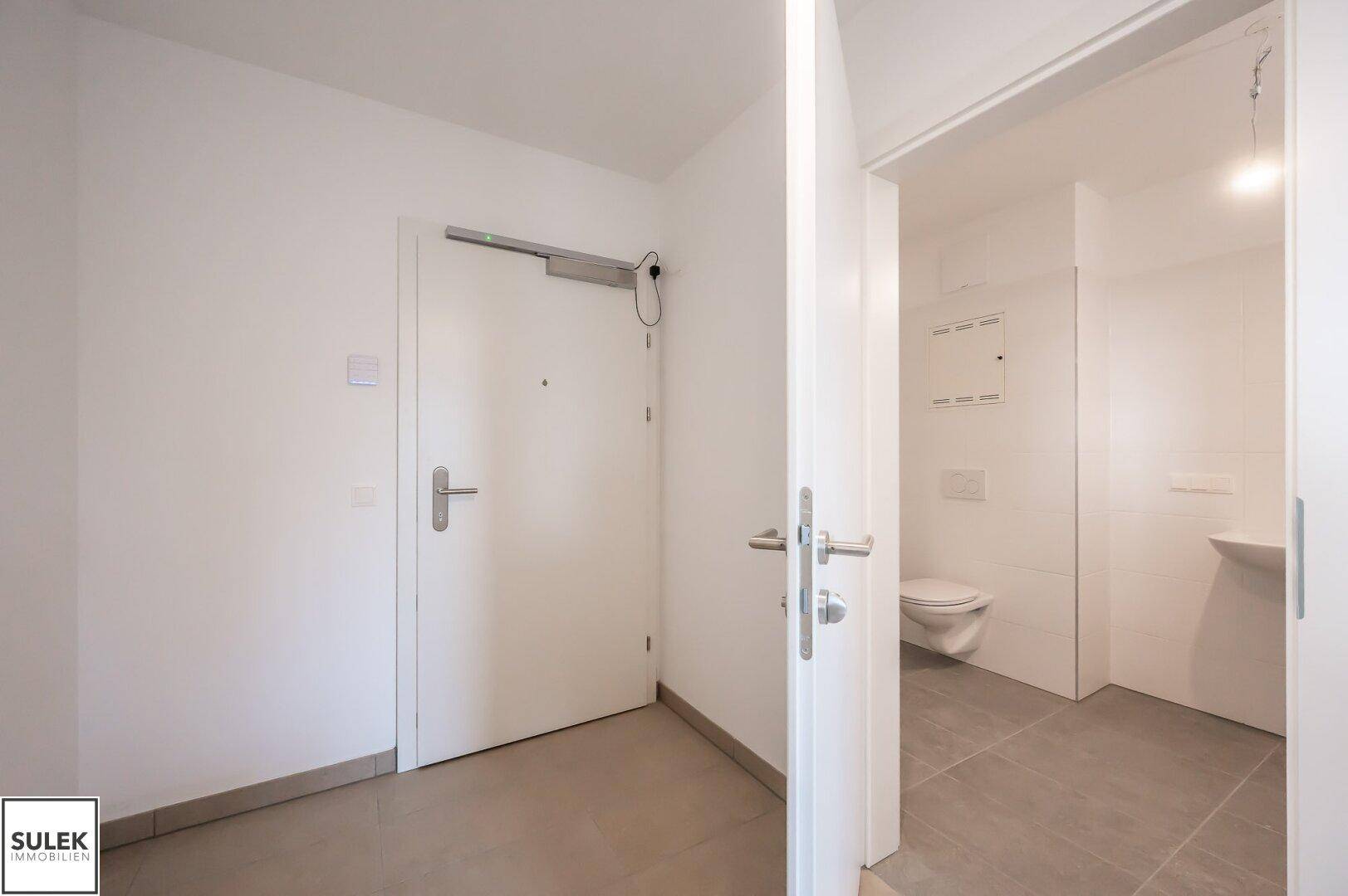 Eingangsbereich mit heller Fliese und Blick in das angrenzende Badezimmer.