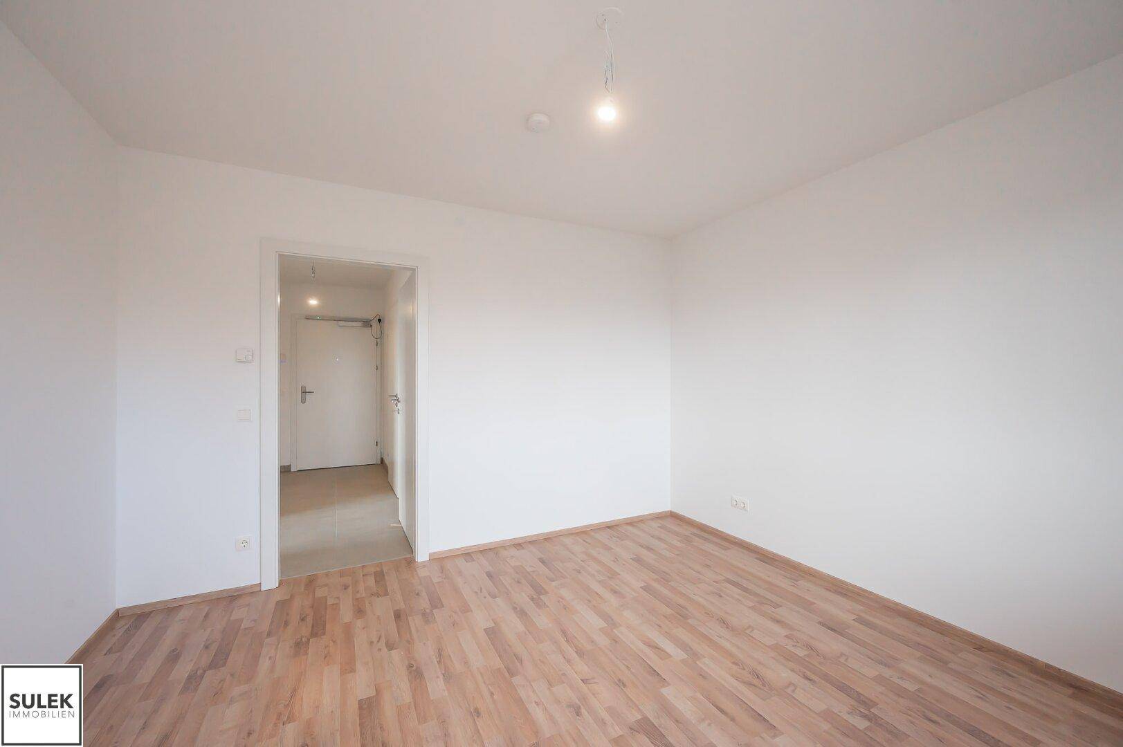 Helles Zimmer mit Laminatboden und Zugang zu einem weiteren Raum, ideal als Schlafzimmer.