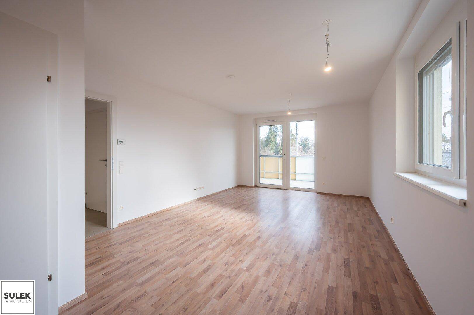 Heller Wohnbereich mit Laminatboden und Zugang zu einem Balkon, ideal für gemütliche Stunden.