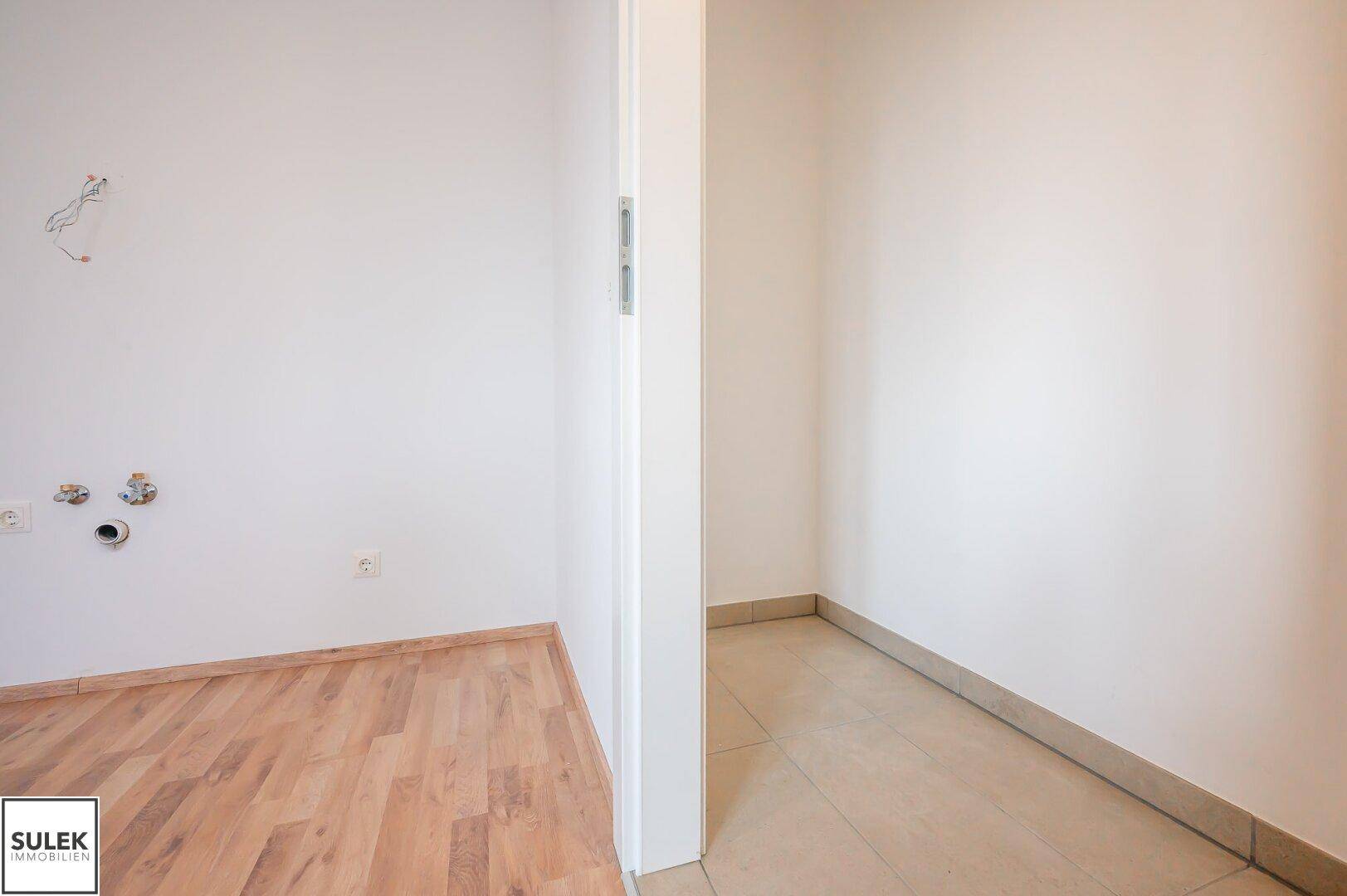 Ecke eines Raumes mit Laminatboden und Blick in einen gefliesten Nebenraum.