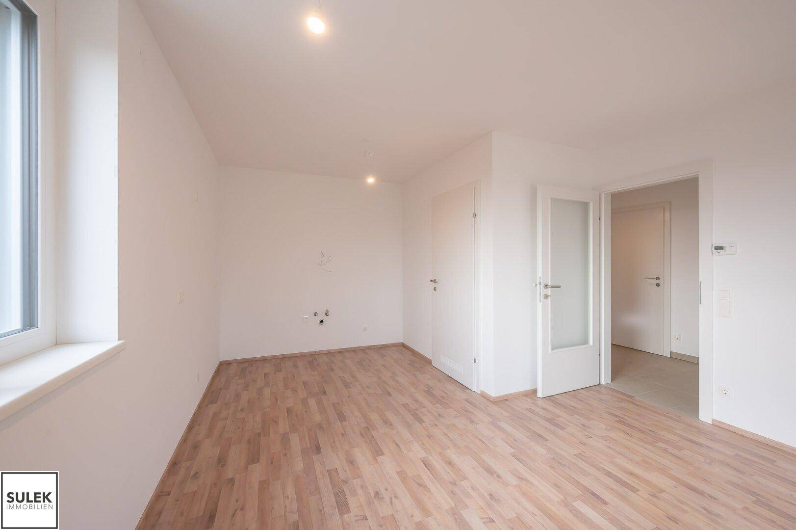 Leerer Raum mit Laminatboden und Anschlüssen an der Wand, vielseitig nutzbar.