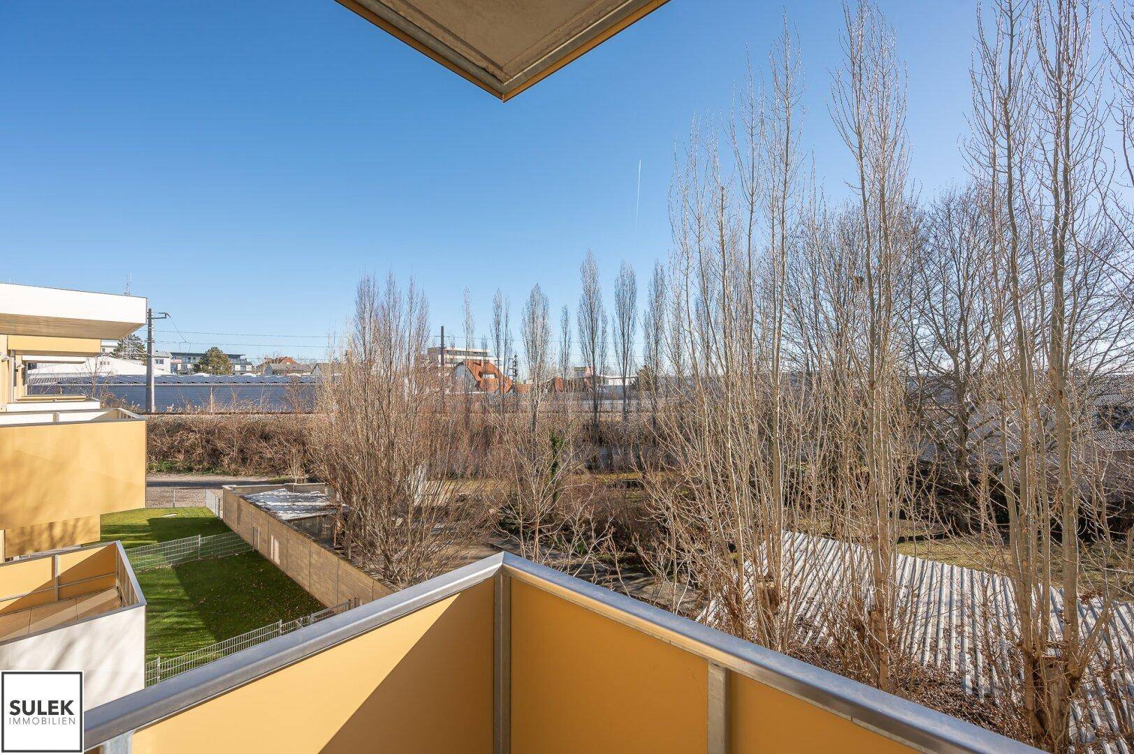Weitläufiger Blick von einem Balkon auf die umliegende grüne Landschaft und Gebäude.