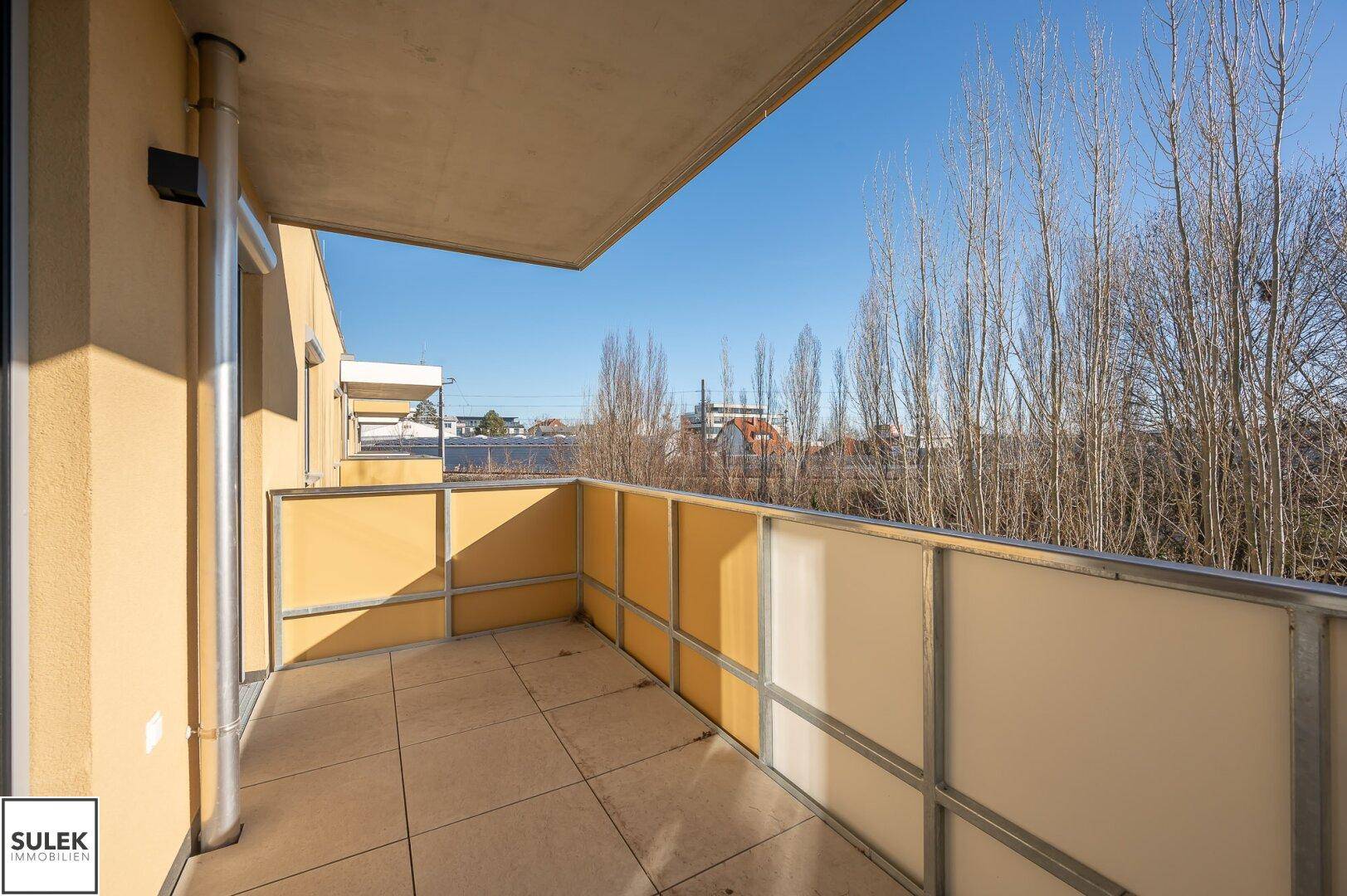Heller Balkon mit Fliesenboden und seitlichem Sichtschutz, bietet Platz für Erholung im Freien.