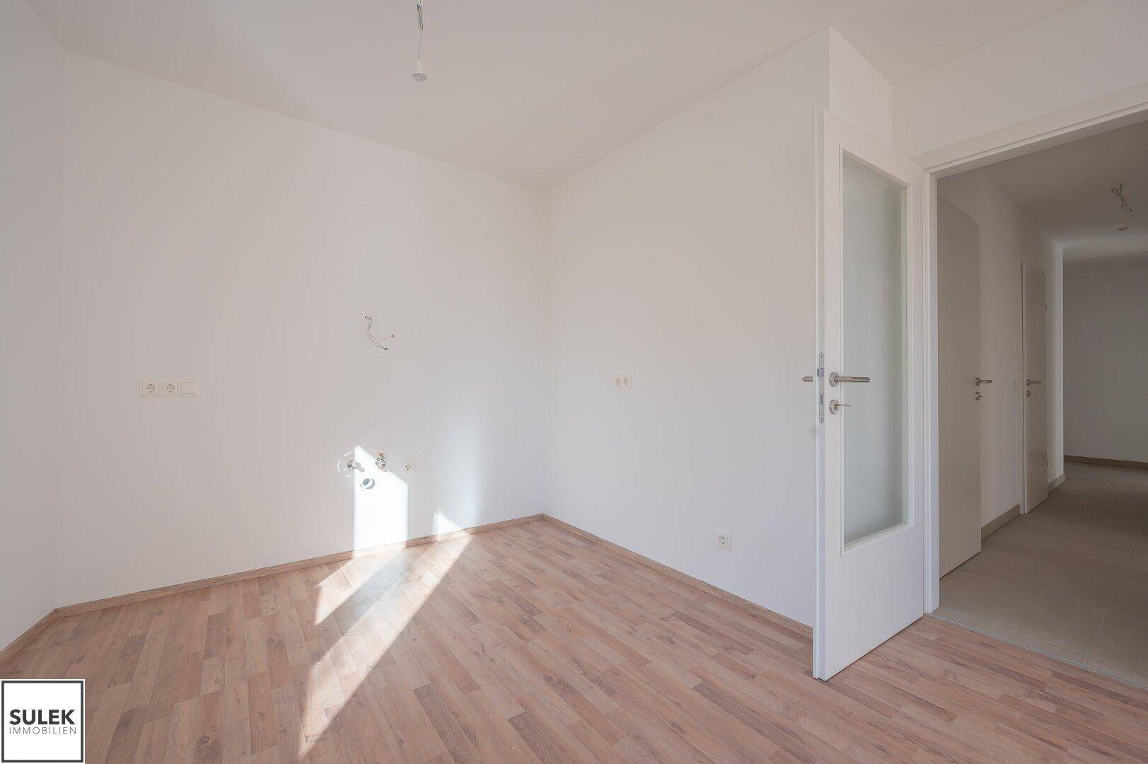 Leerer Raum mit hellem Laminatboden und weißen Wänden, bereit zur individuellen Gestaltung.