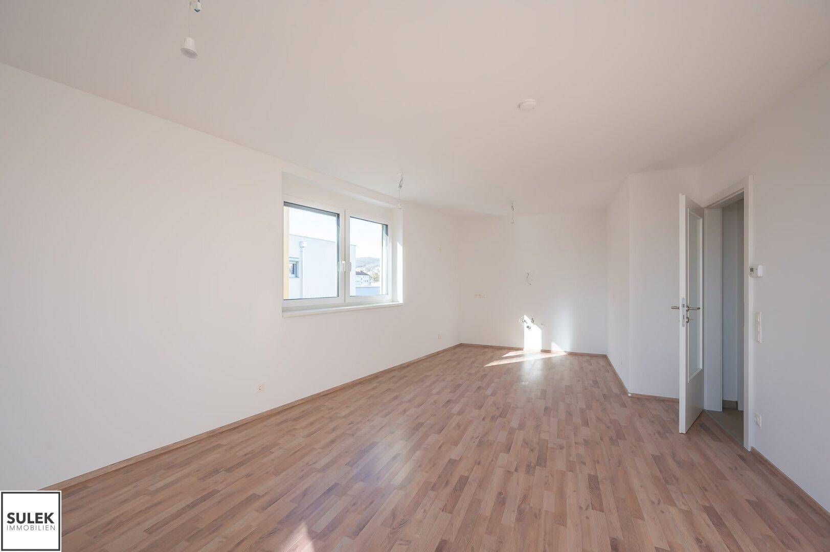 Geräumiger, heller Raum mit Laminatboden und großem Fenster, bietet viel Tageslicht.