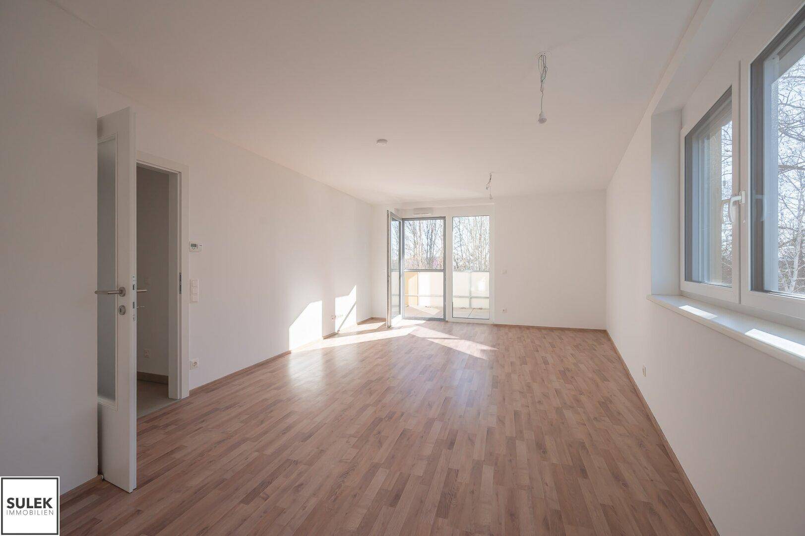 Großzügiger, lichtdurchfluteter Raum mit Laminatboden und Zugang zum Balkon, ideal für Wohnbereiche.