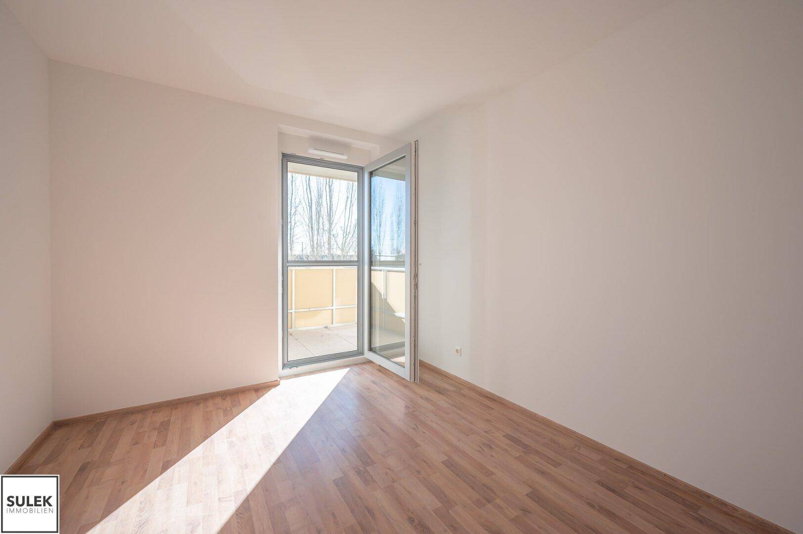 Helles Zimmer mit Laminatboden und Balkonzugang, bietet viel Tageslicht und frische Luft.