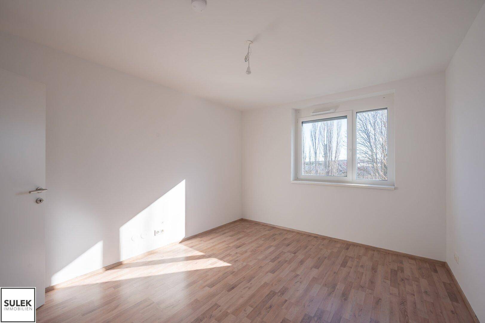 Leeres Zimmer mit Laminatboden und Fenster, bietet viel Potenzial für ein Schlafzimmer oder Büro.
