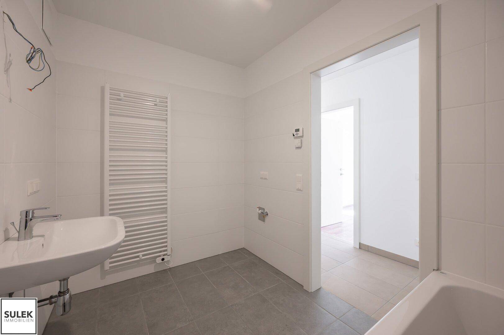 Modernes Badezimmer mit weißen Fliesen, Waschbecken und Handtuchheizkörper, bereit zur Nutzung.