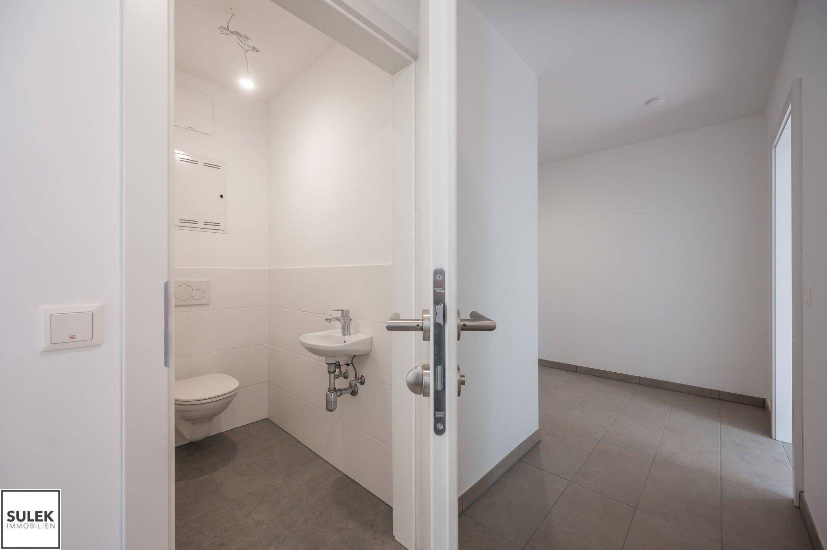 Separates Gäste-WC mit wandhängender Toilette und kleinem Waschbecken, funktional und hell.