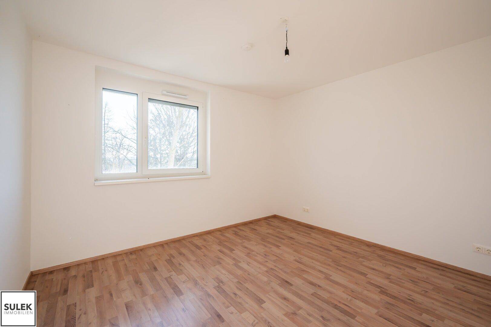 Helles Zimmer mit Laminatboden und einem Fenster, das viel Tageslicht hereinlässt.
