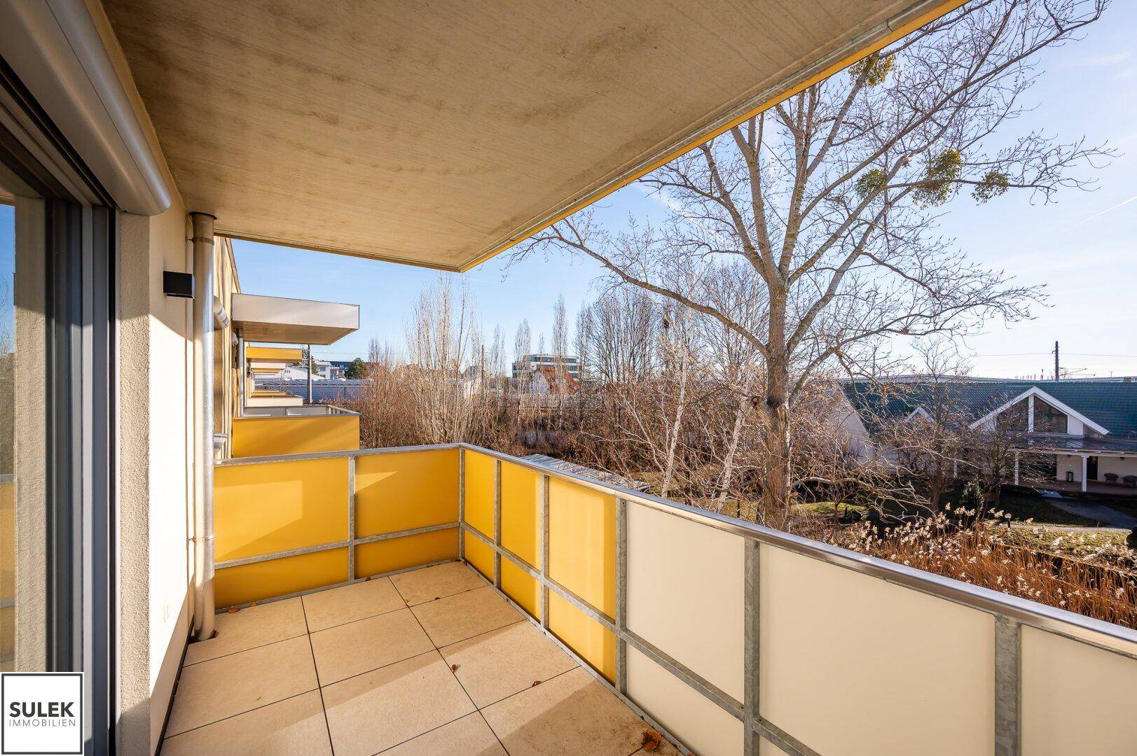 Geräumiger Balkon mit gelben Paneelen und weitem Blick ins Grüne.