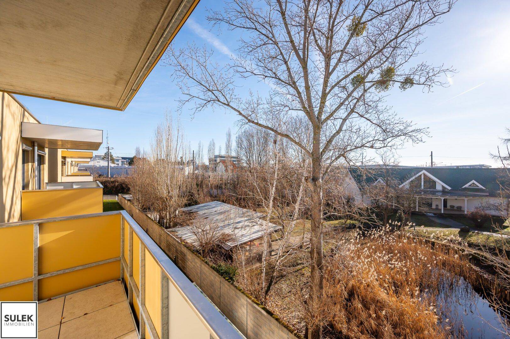 Sonniger Balkon mit Blick auf einen Teich und die umliegende Natur.