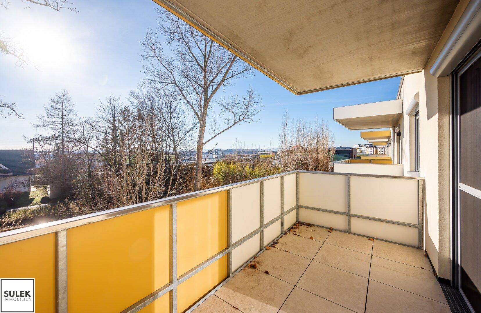 Heller Balkon mit gelben und weißen Sichtschutzpaneelen und weitem Ausblick.