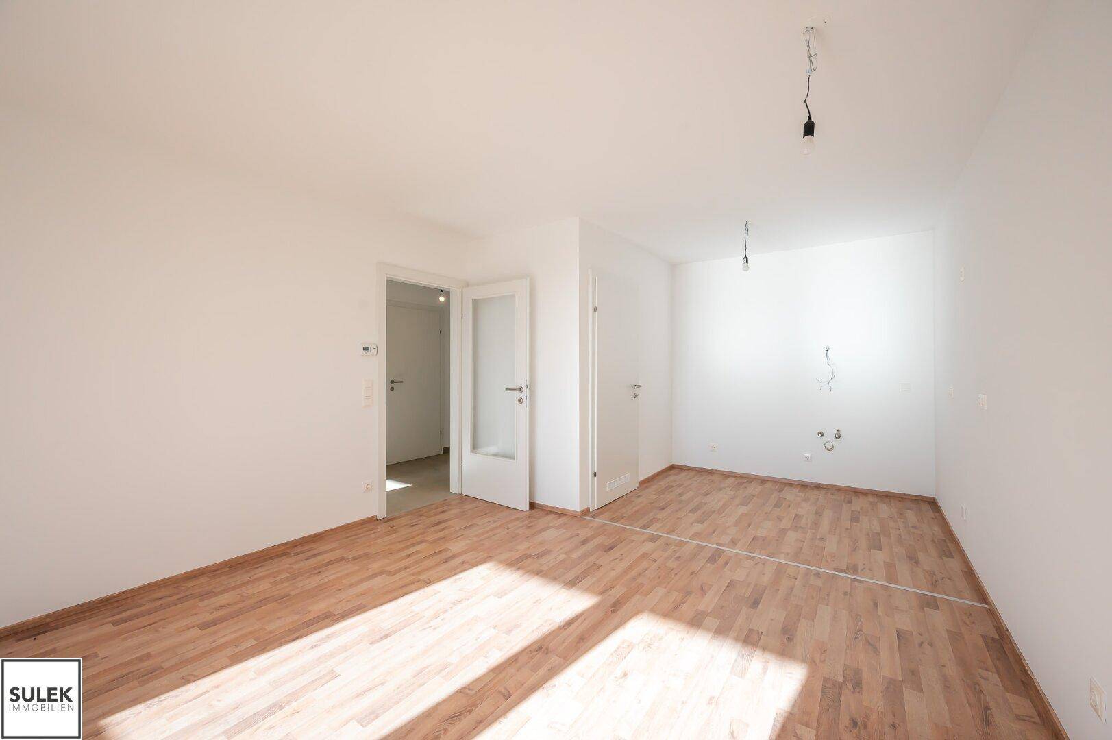 Geräumiges Wohnzimmer mit Laminatboden und vorbereiteten Anschlüssen für die Küche.