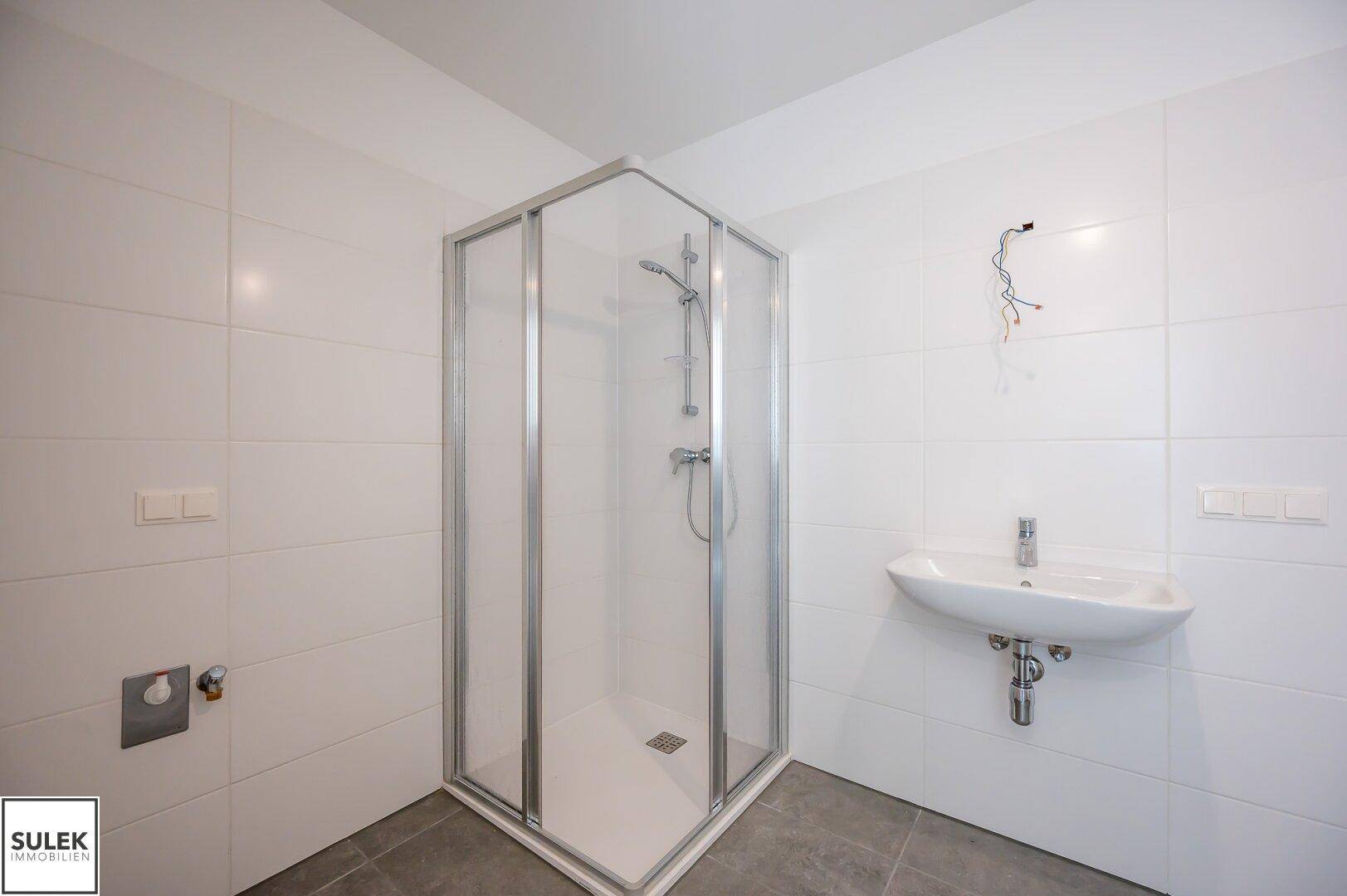 Helles Badezimmer mit Eckdusche, Waschbecken und weißen Wandfliesen.