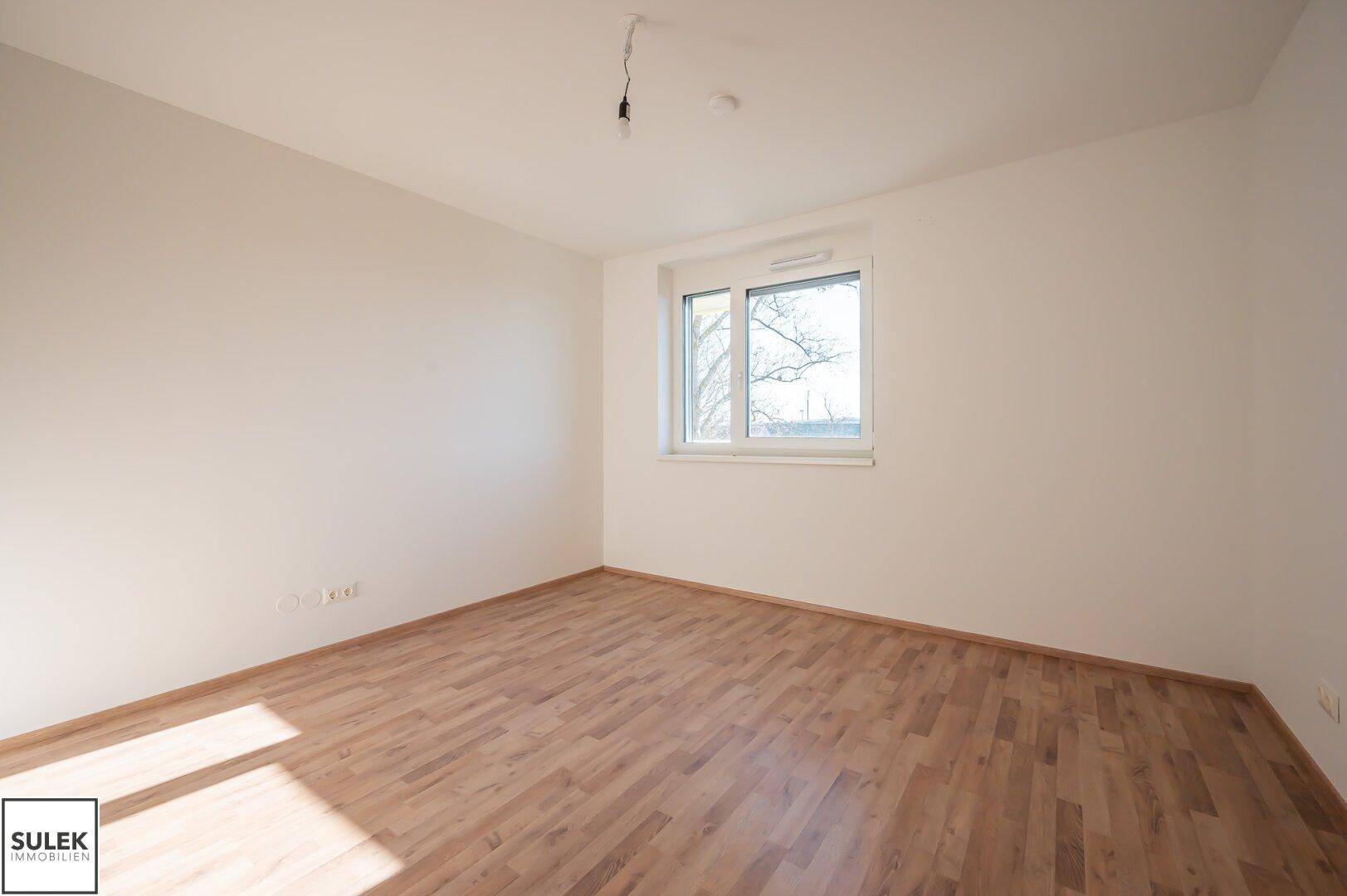 Geräumiges Schlafzimmer mit Laminatboden und einem großen Fenster.
