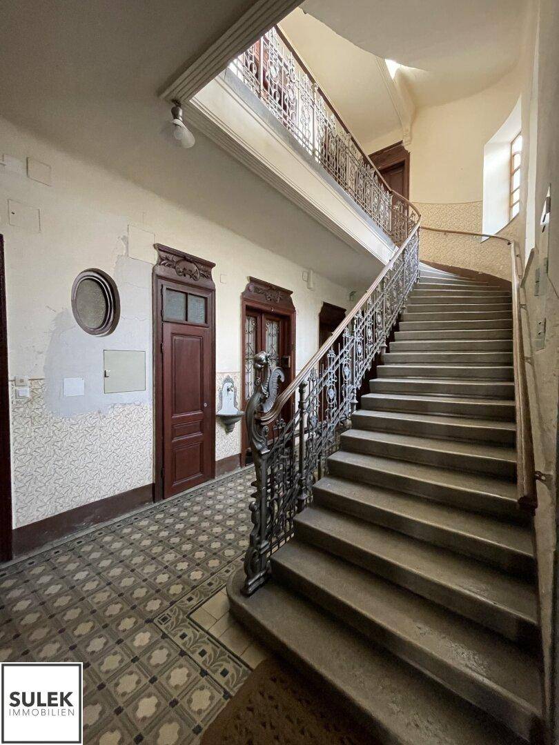 Großes Treppenhaus mit schmiedeeisernem Geländer, hohen Decken und natürlichem Lichteinfall.