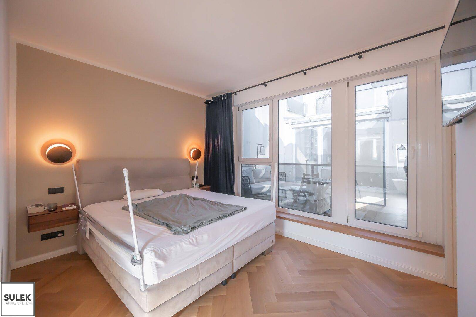 Helles Schlafzimmer mit Doppelbett, Parkettboden und Zugang zur Terrasse.