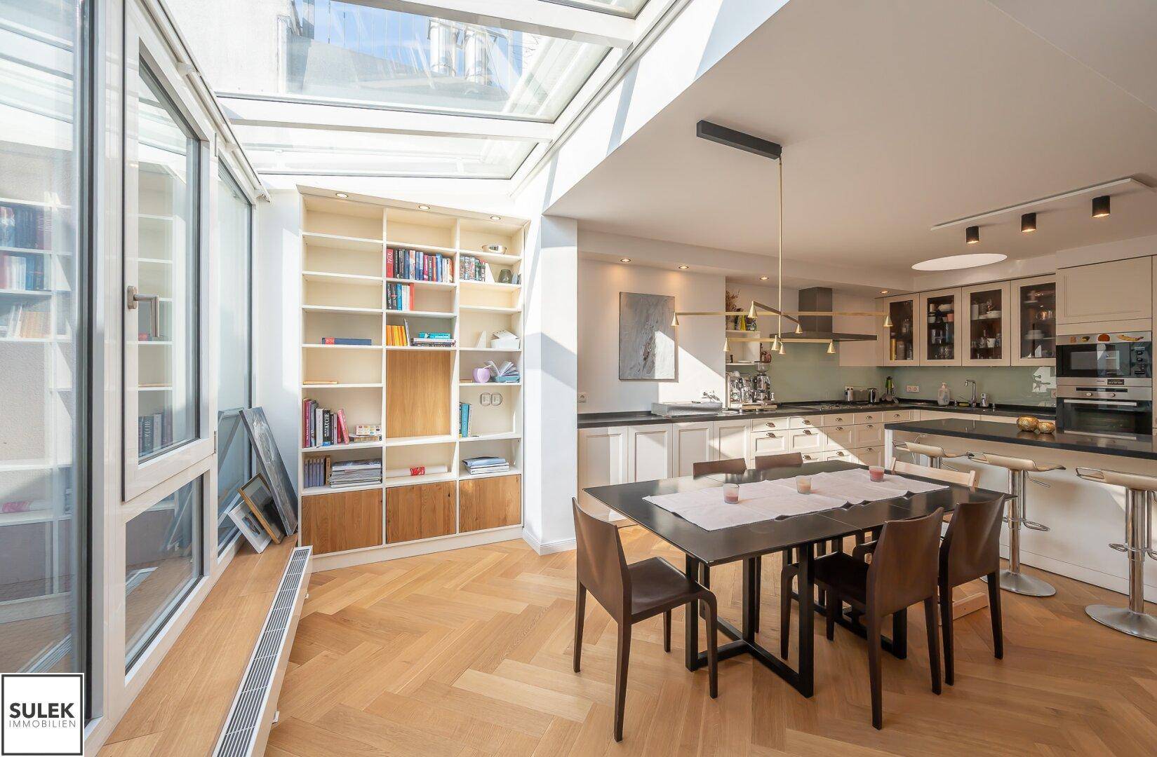 Helle Küche mit Essbereich, Einbauregalen und großzügiger Glasfront.