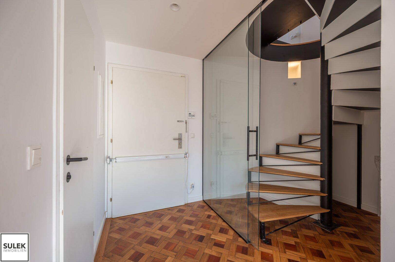 Eingangsbereich mit Holzboden und eleganter Wendeltreppe mit Glasgeländer.