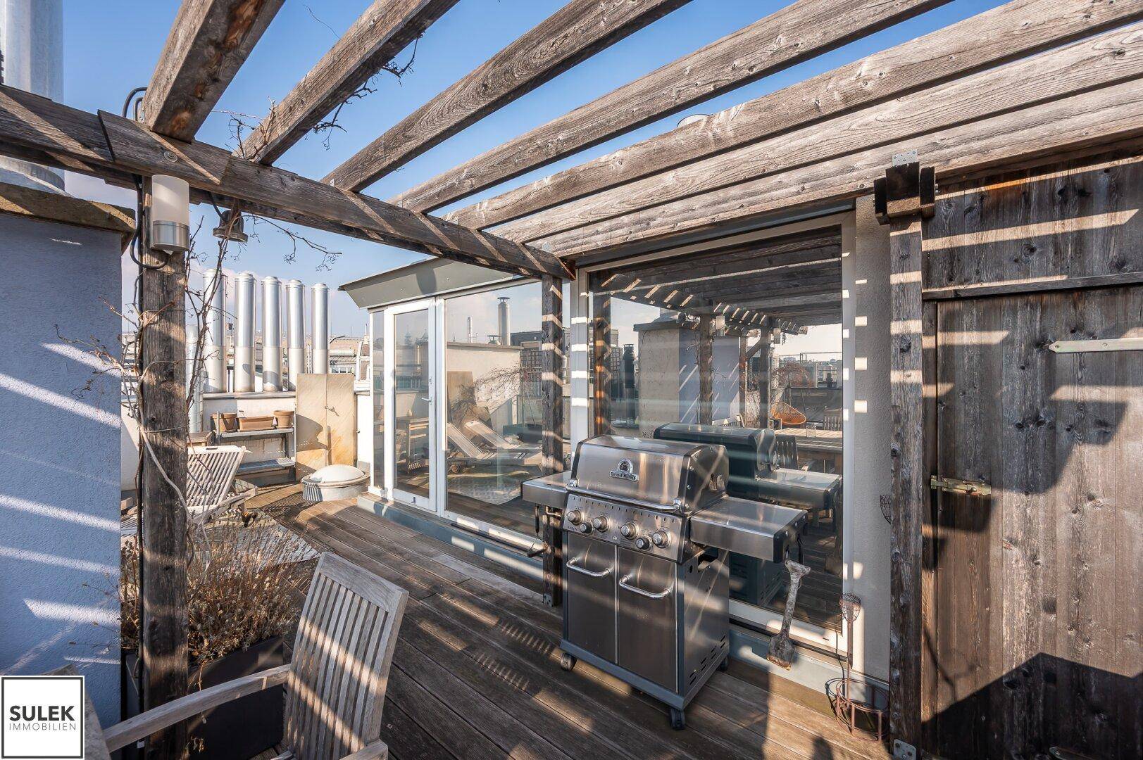 Sonniger Dachgarten mit Holzpergola, Grillbereich und Sitzgelegenheiten.