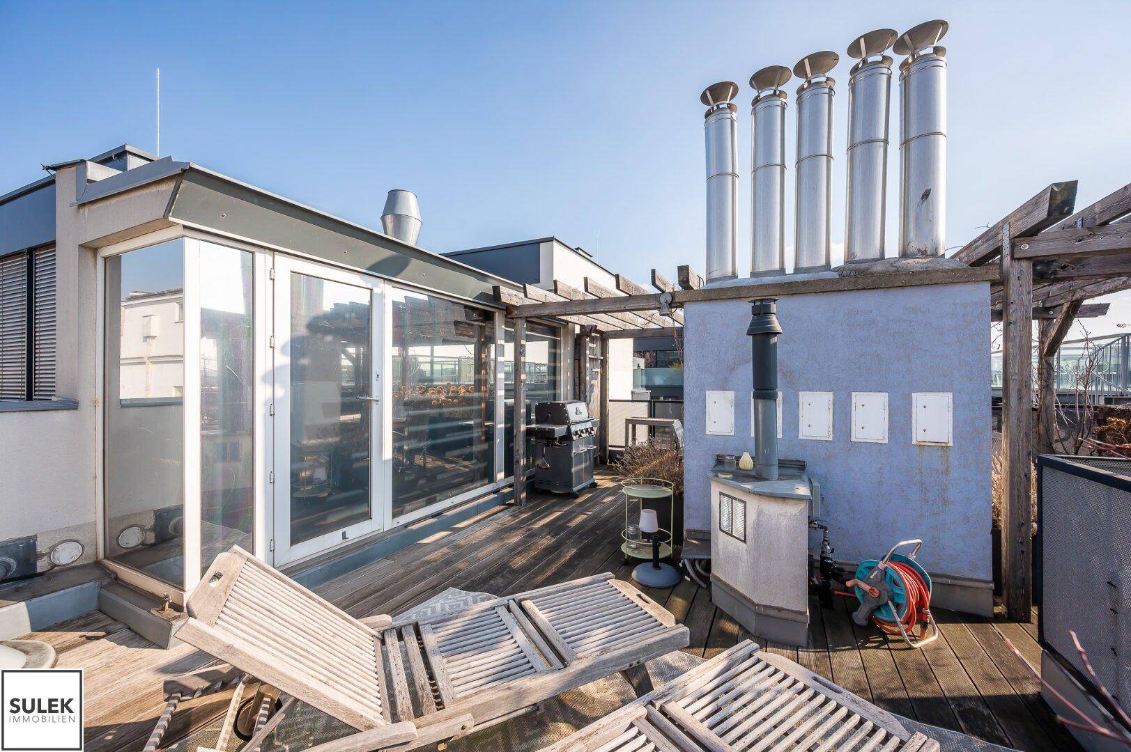 Geräumige Dachterrasse mit Liegestühlen, Grill und Blick auf die Umgebung.