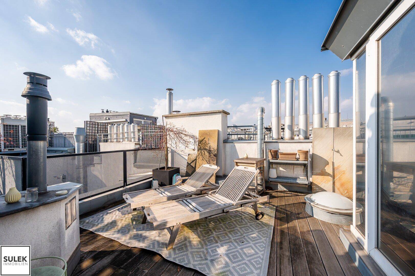 Gemütliche Dachterrasse mit Liegestühlen, Teppich und Blick über die Dächer.