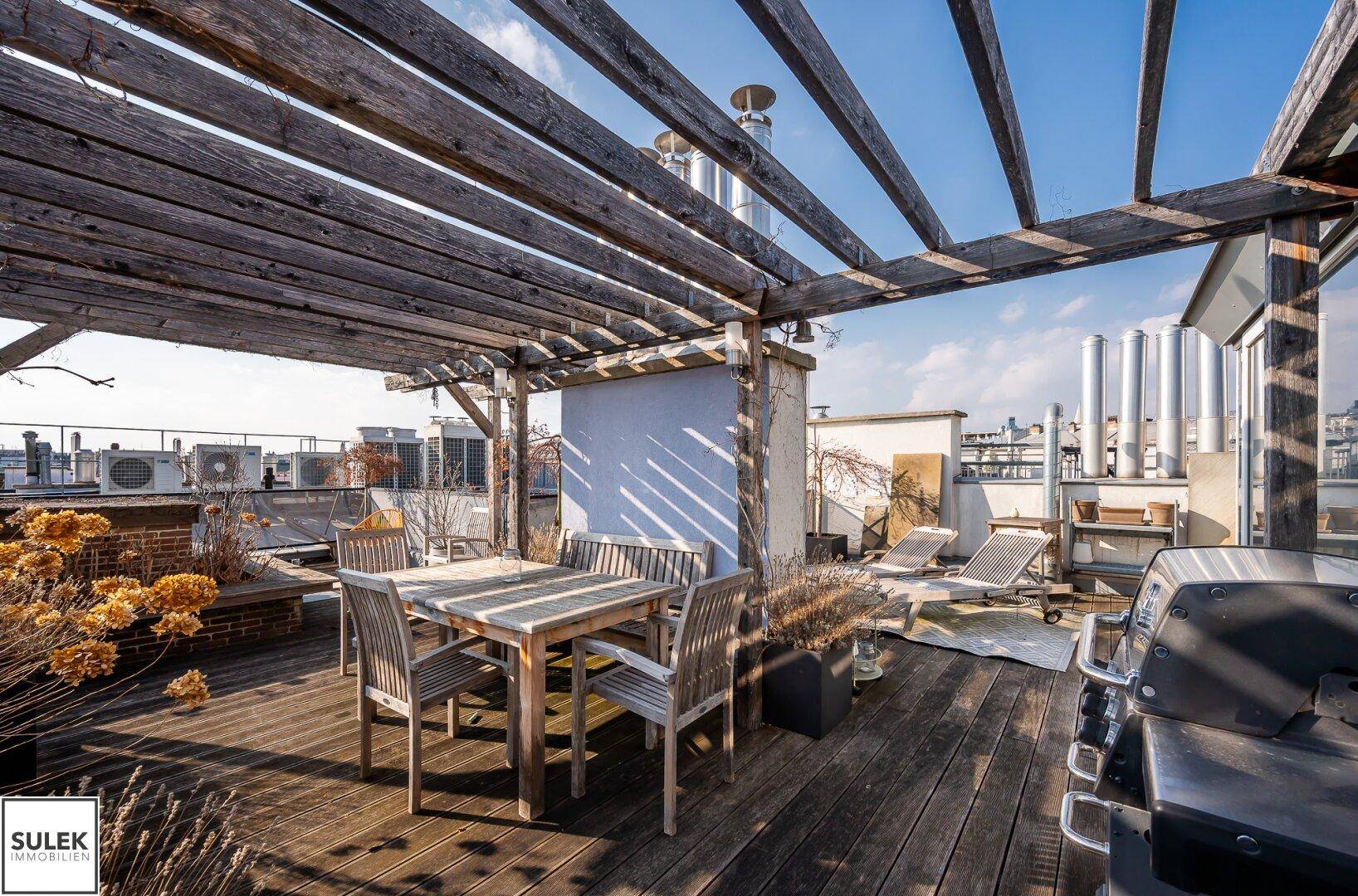 Sonniger Dachgarten mit Holzpergola, Esstisch und Grillbereich.
