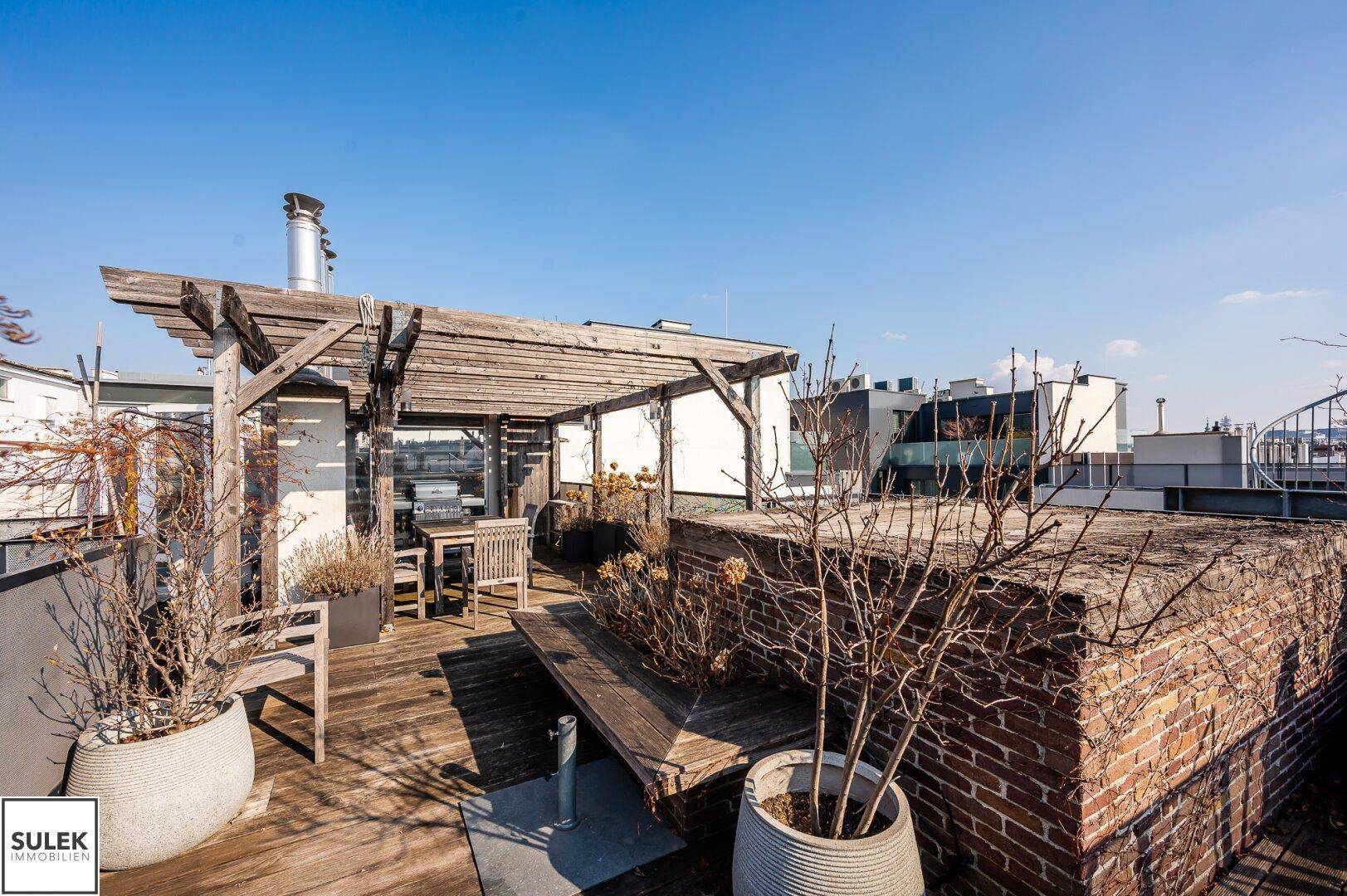 Dachterrasse mit Holzpergola, gemauertem Pflanzbeet und Topfpflanzen.