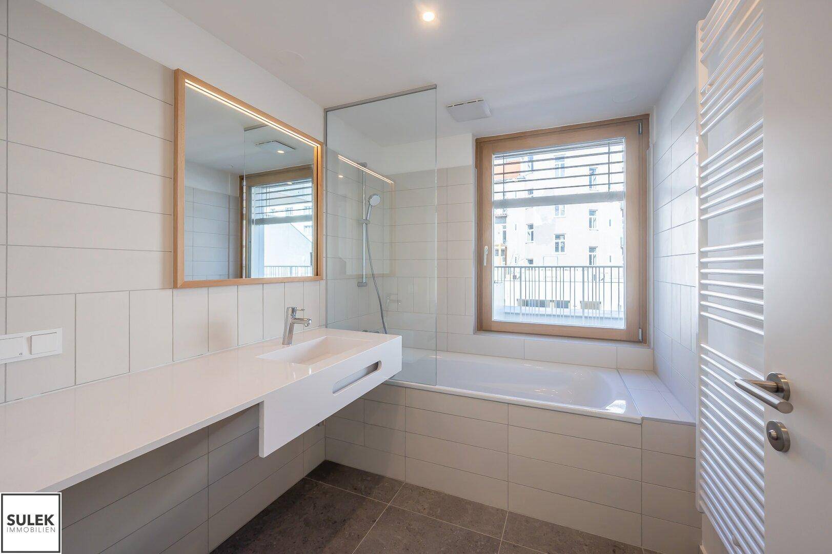 Modernes Badezimmer mit Badewanne, integriertem Waschtisch und einem Fenster für Tageslicht.