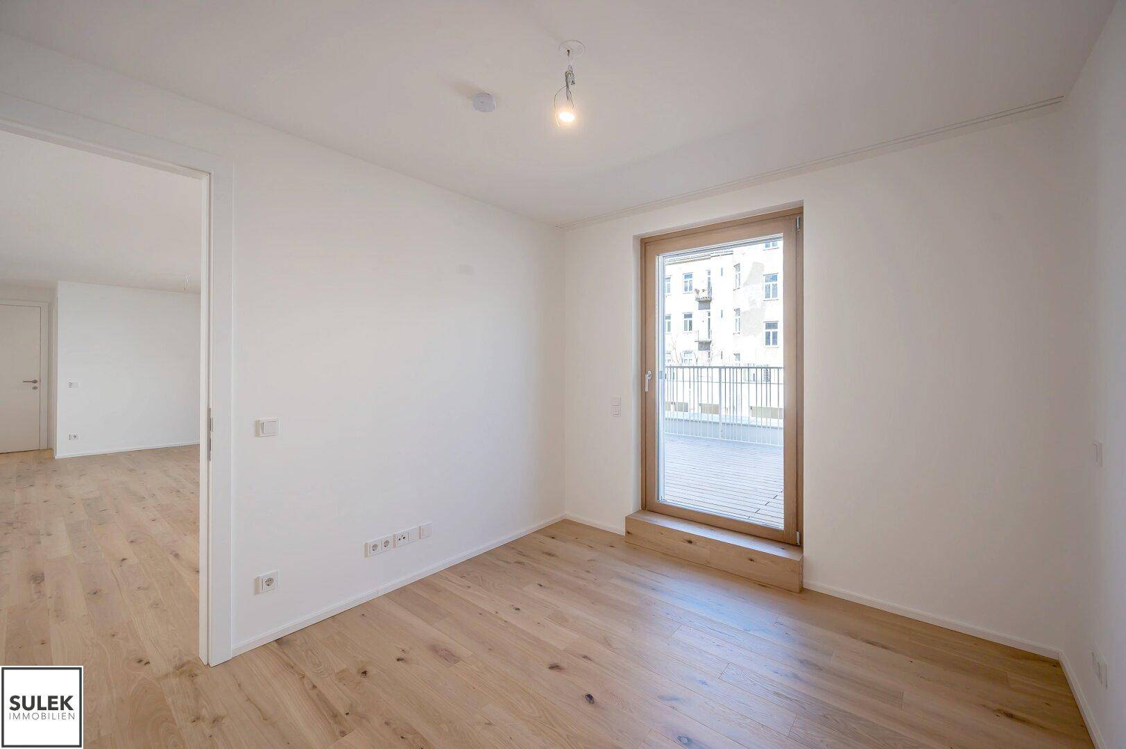Helles Schlafzimmer mit Holzboden und Zugang zu einer Außenterrasse durch eine große Glastür.