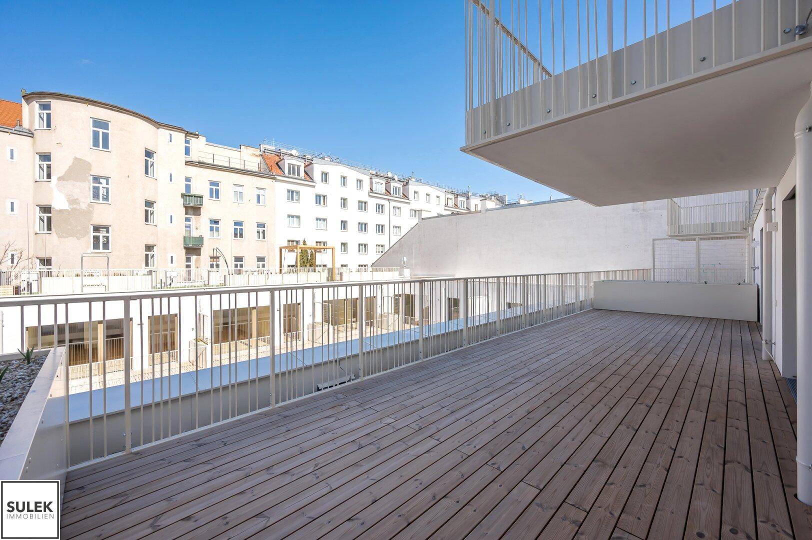 Weitläufige Holzterrasse mit Metallgeländer und Blick auf die umliegende Stadtbebauung.