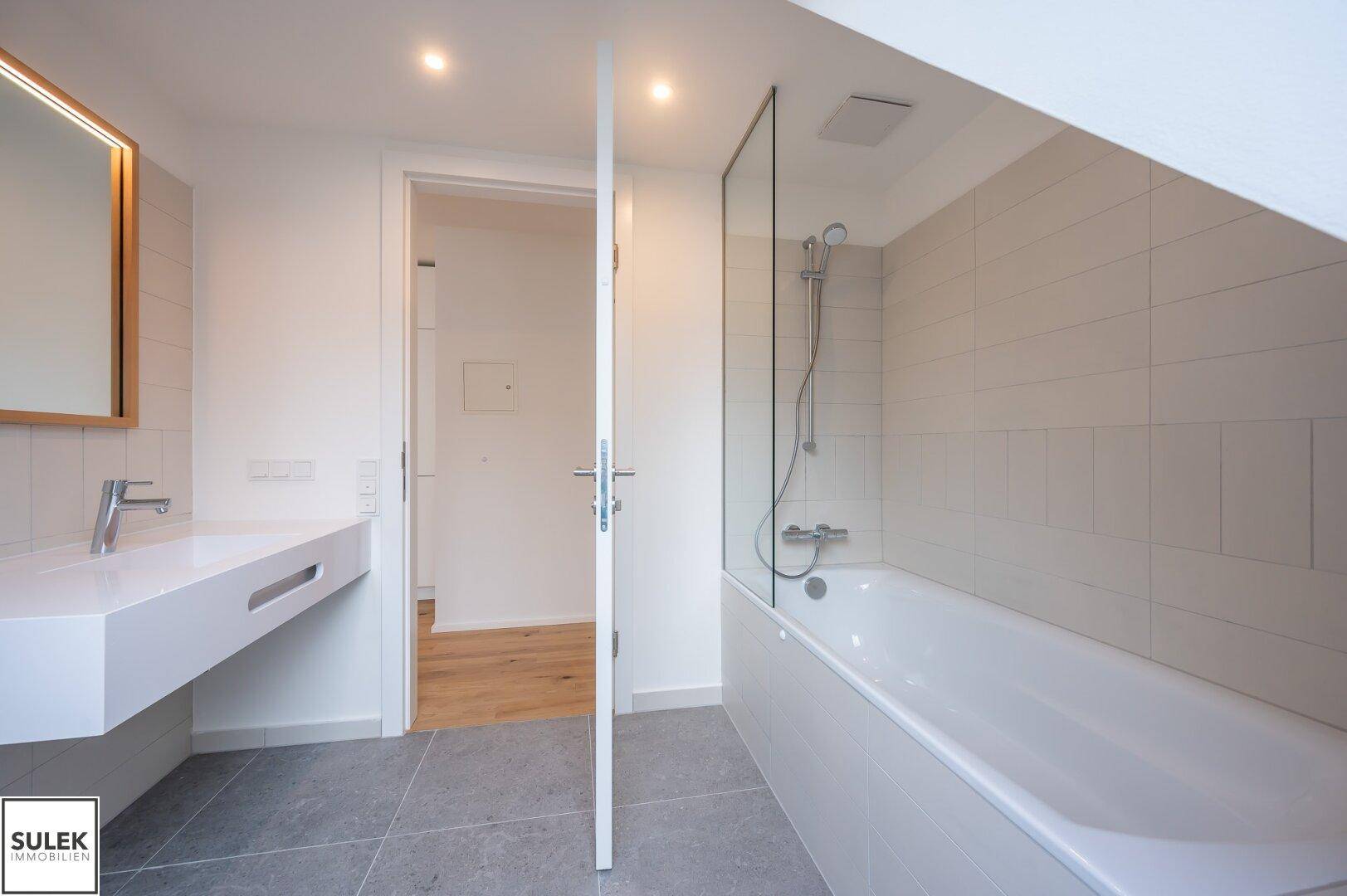 Helles Badezimmer mit Badewanne, Duschabtrennung und modernem Waschtisch unter einer Dachschräge.